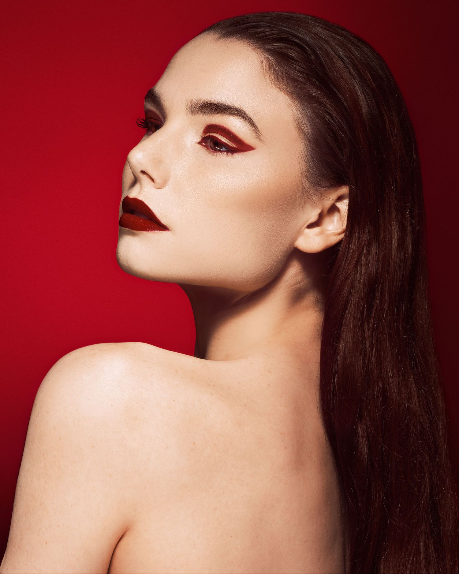 Dramatic beauty portrait with red makeup and dark hair against red background.