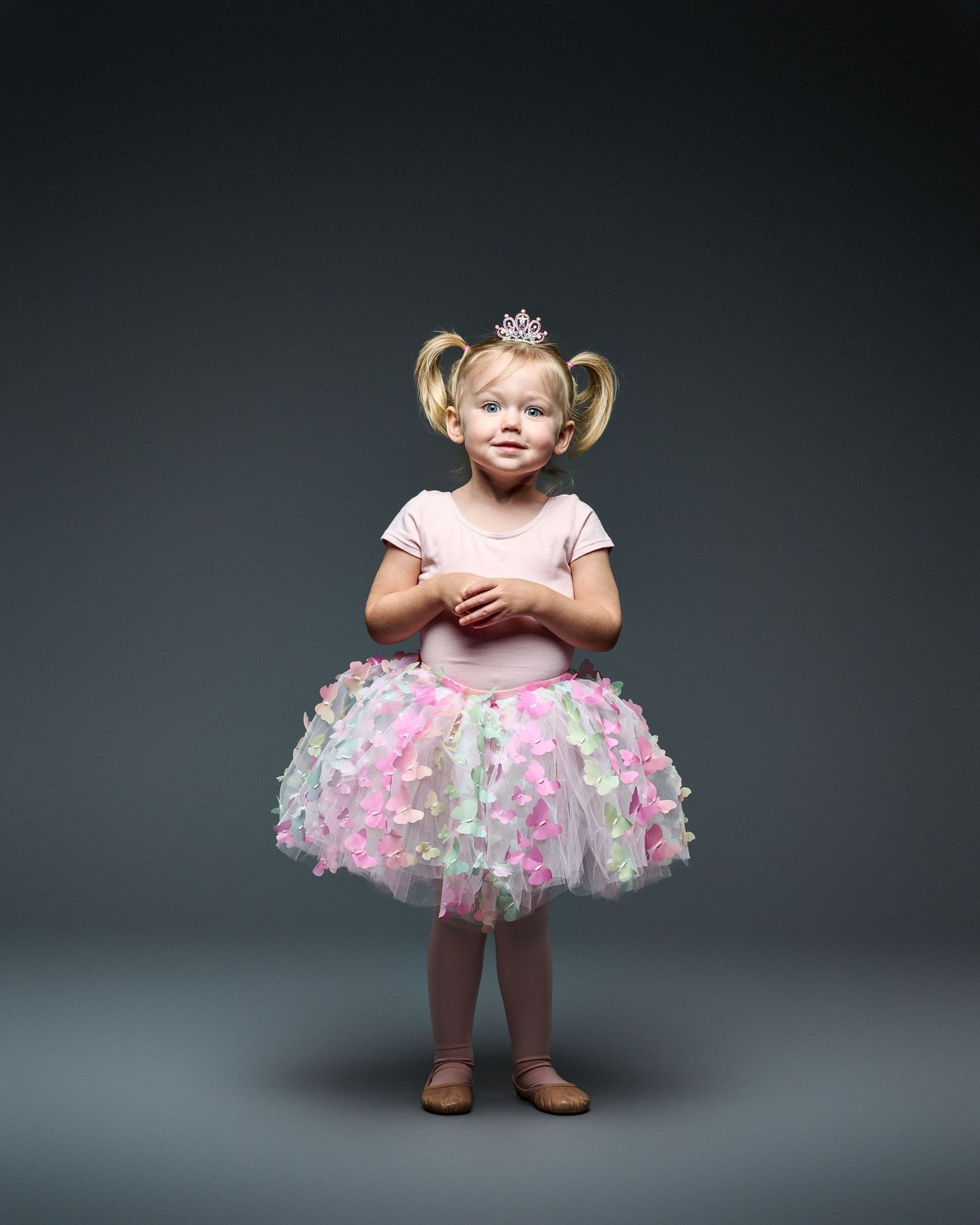 Young dancer in pink tulle tutu and tiara stands ready for ballet class.