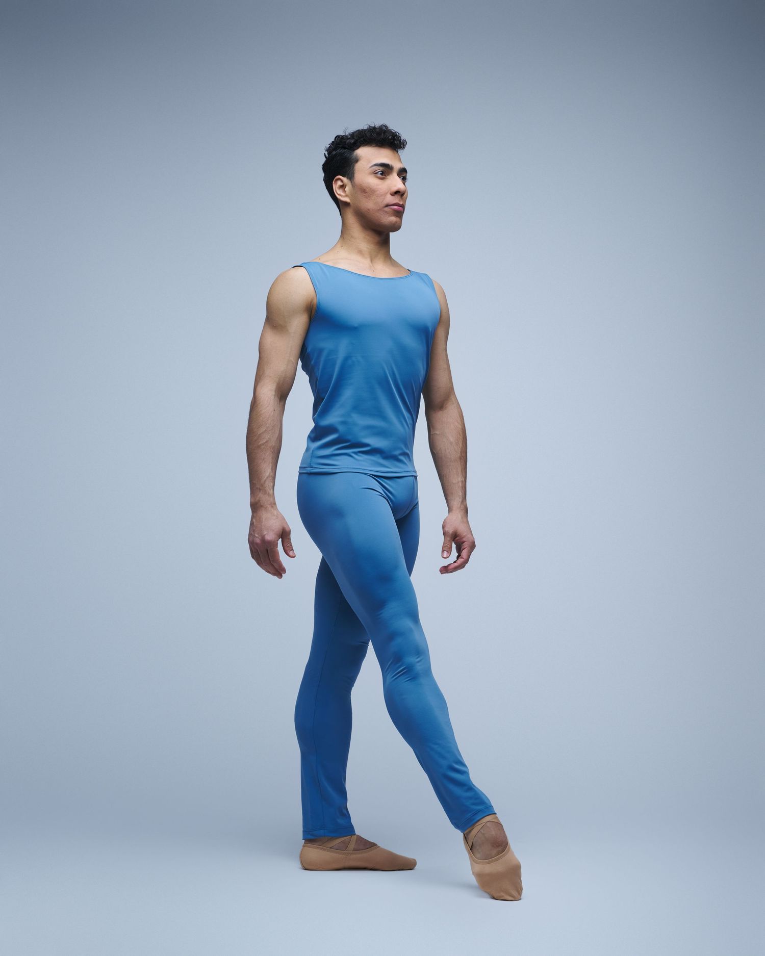 Ballet dancer in light blue leotard strikes elegant pose against studio backdrop.