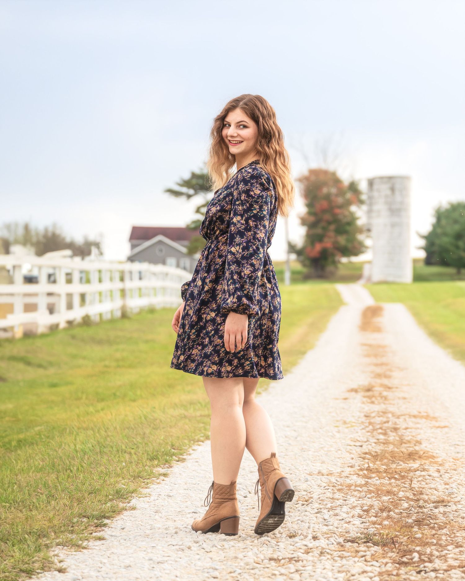 Country scene with floral dress and boots on farm path with white silo.