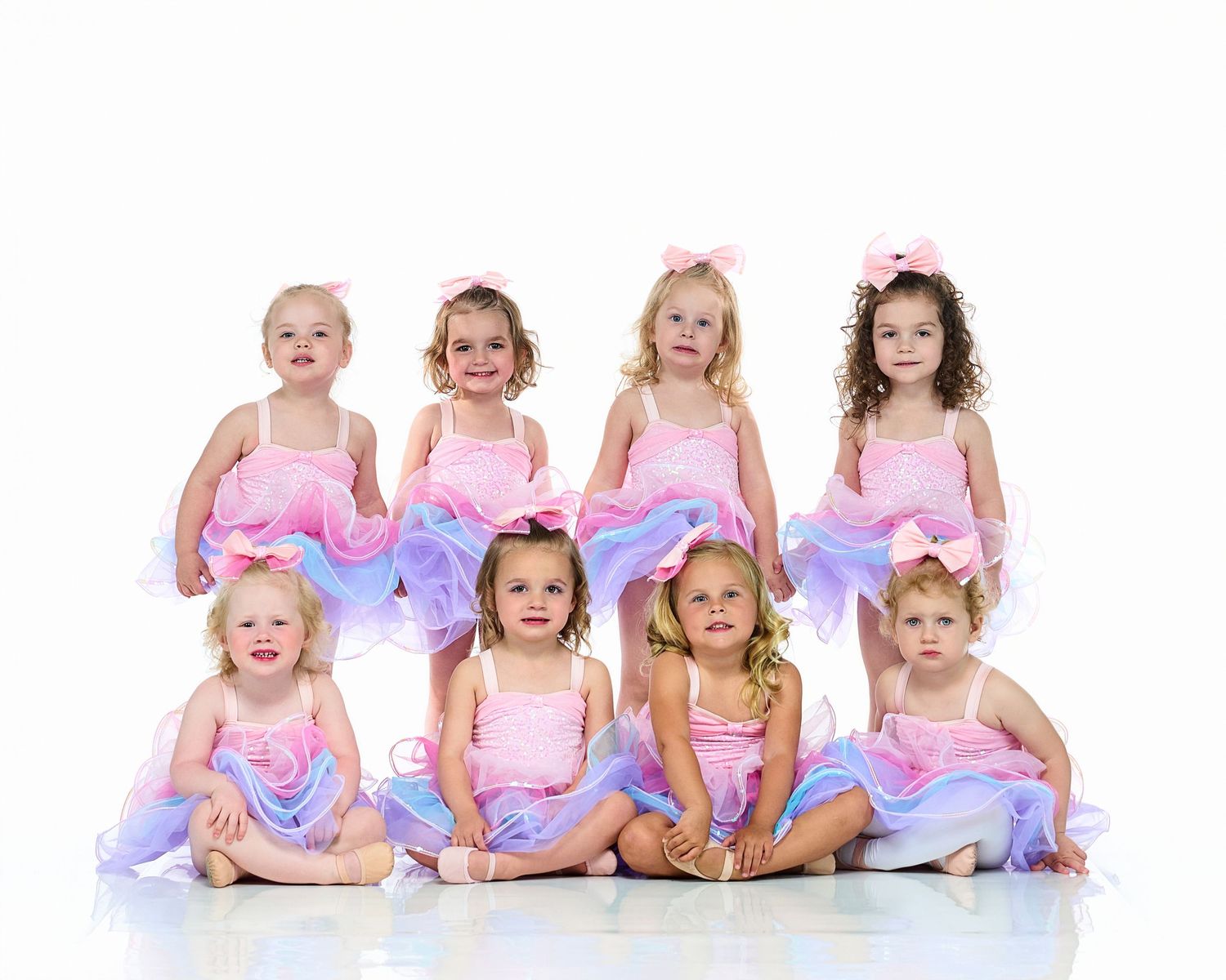 Ballet dancers in pink tutus pose in a graceful seated lineup.