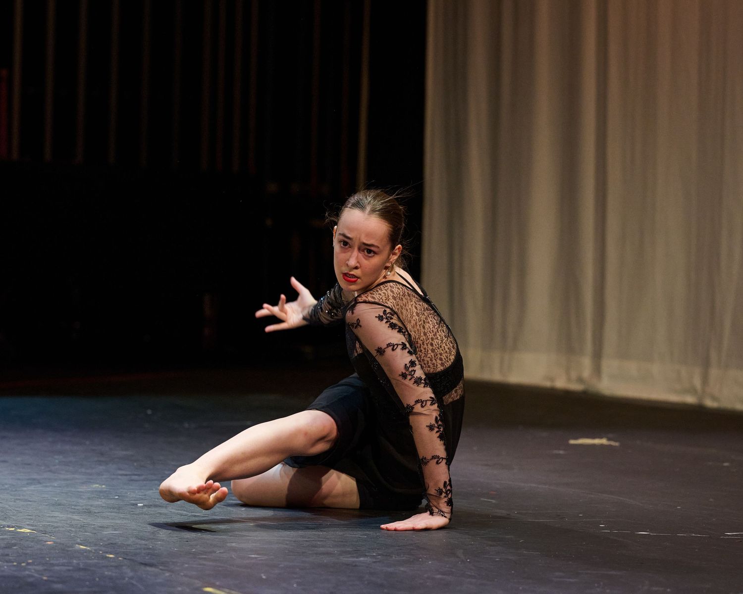 Modern dancer in a sheer black costume performs an emotional solo on a dimly lit stage.