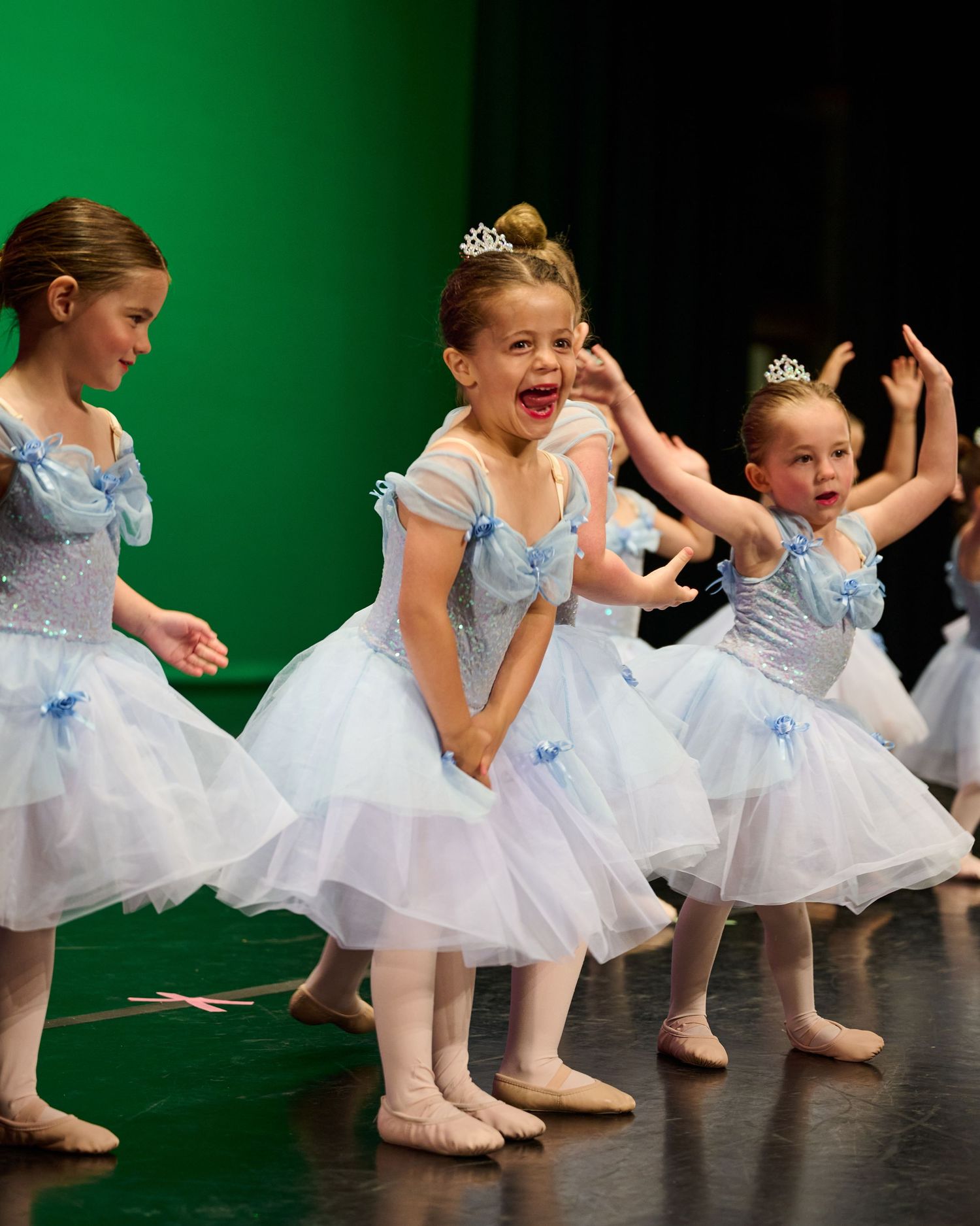 Young ballet dancers in light blue tutus performing animated moves during stage show.
