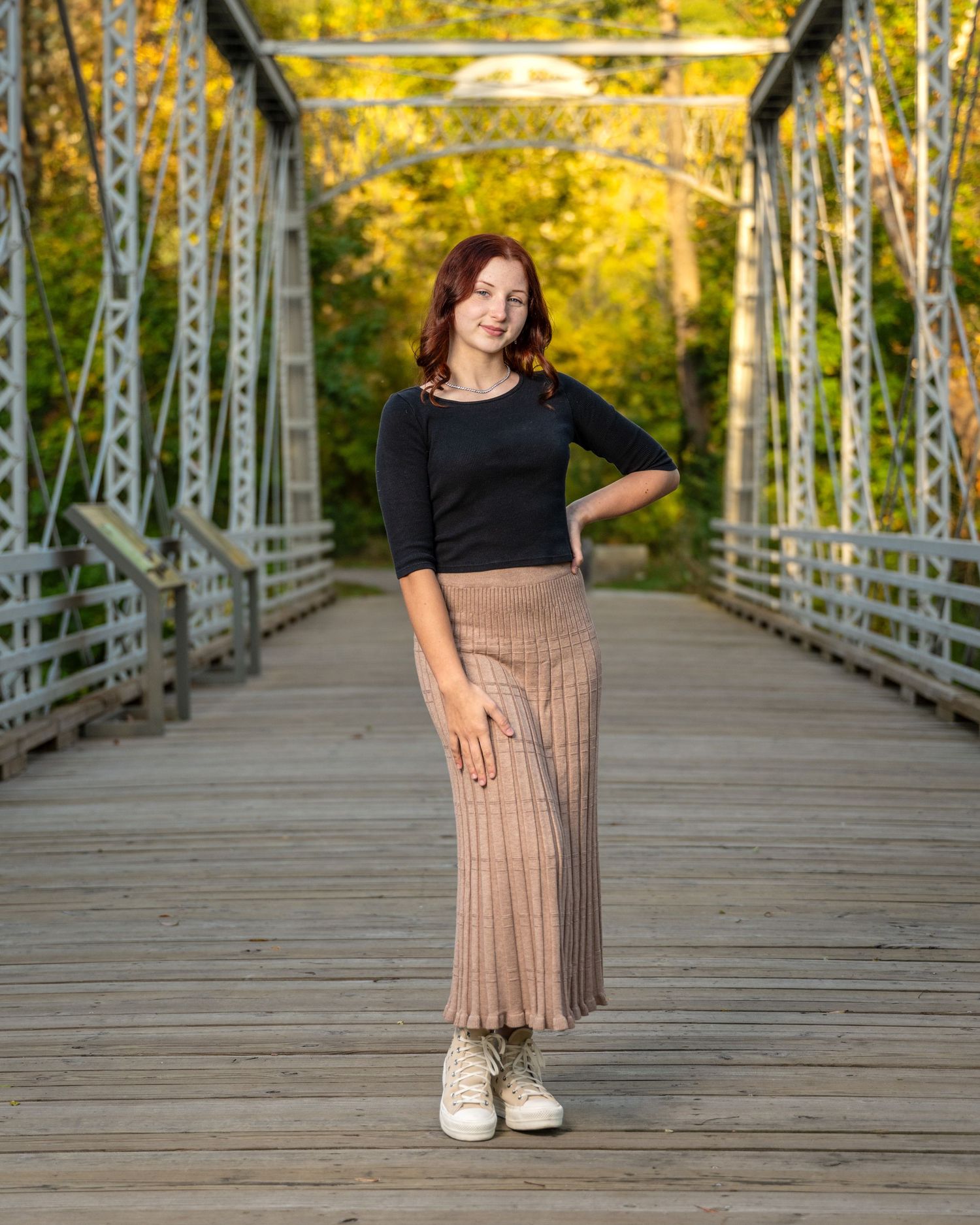 Fall portrait on wooden bridge wearing black top and tan skirt.