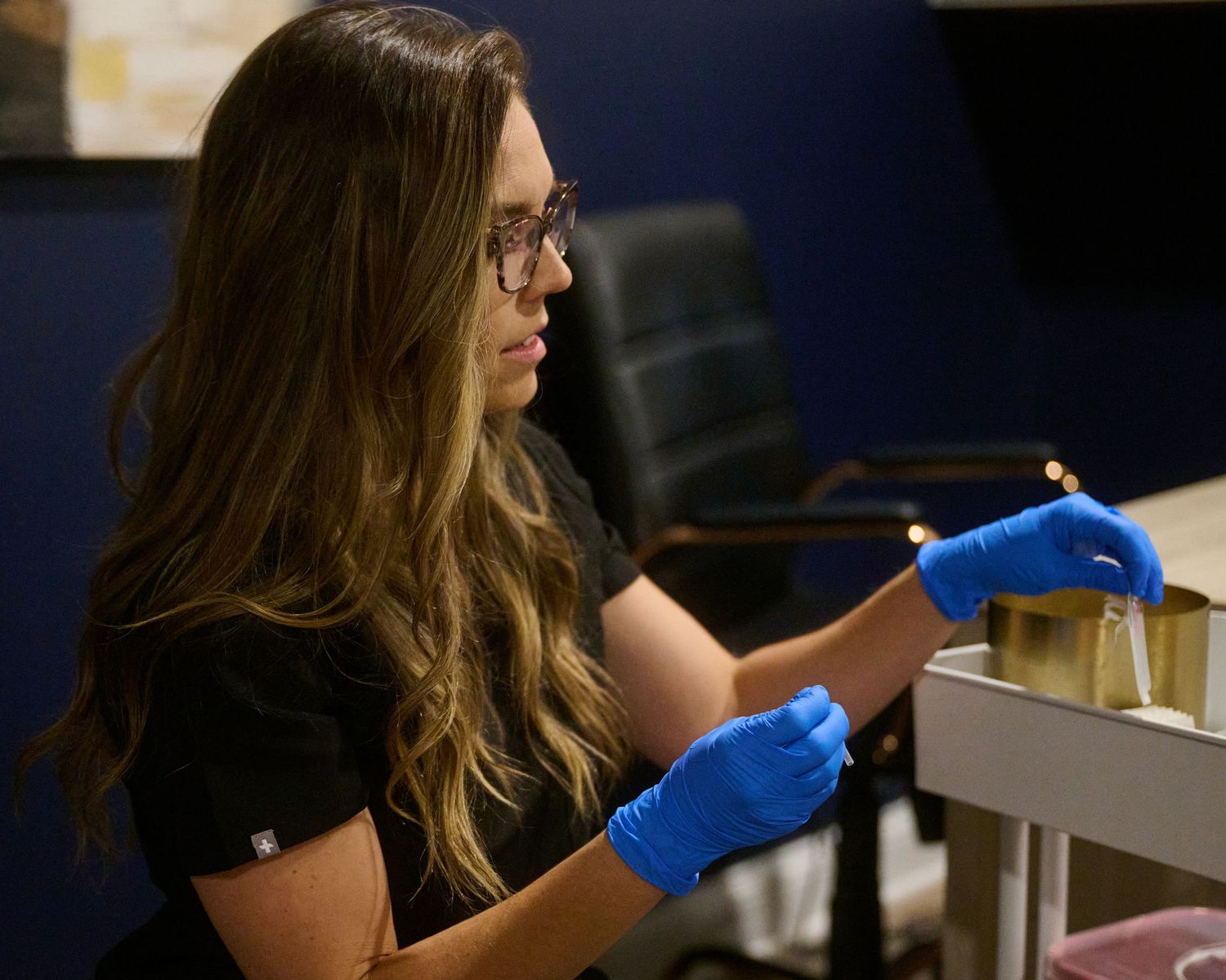 Laboratory researcher wearing blue gloves carefully handles scientific equipment in dark setting.