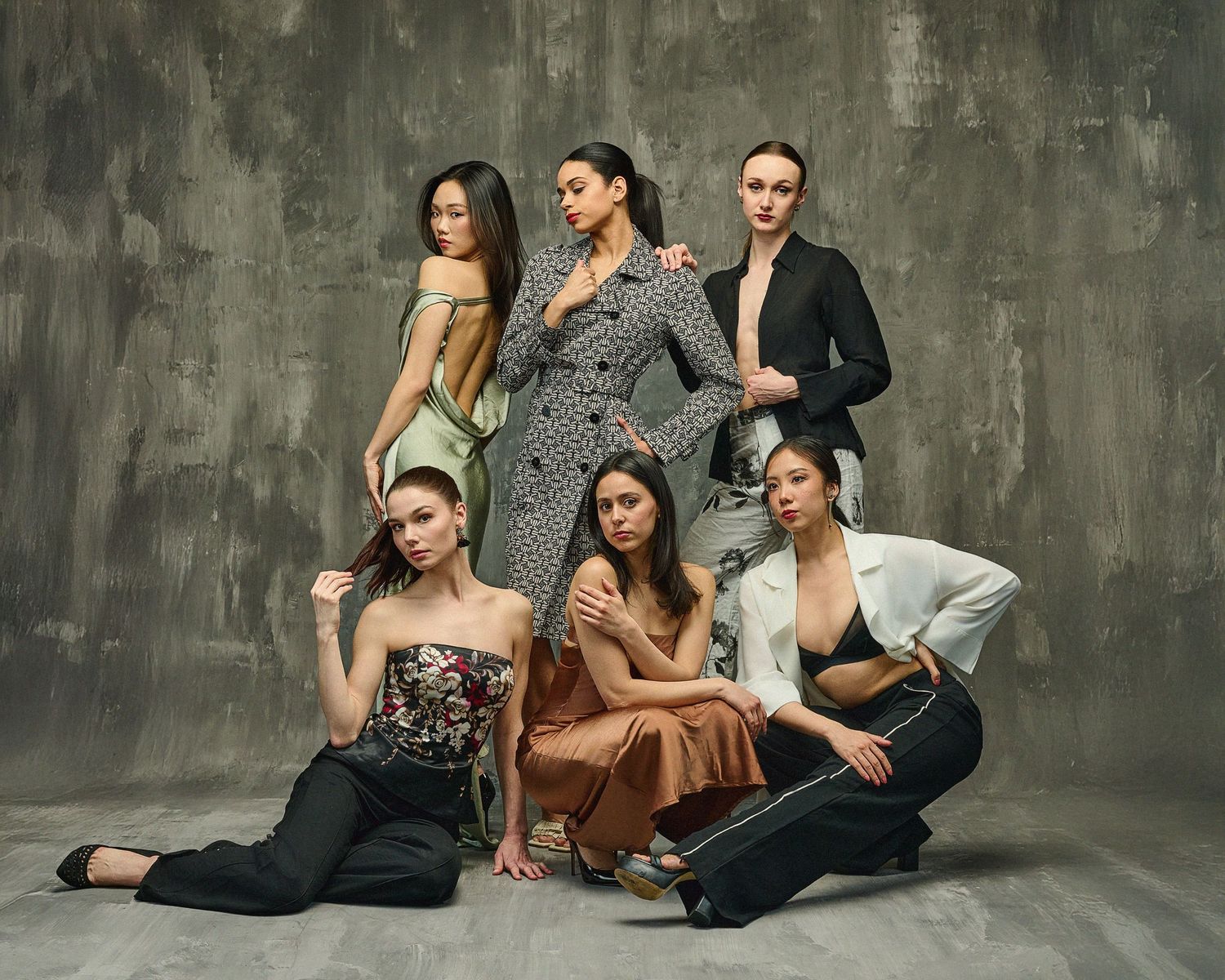 Fashion models in elegant attire posing together against concrete background.