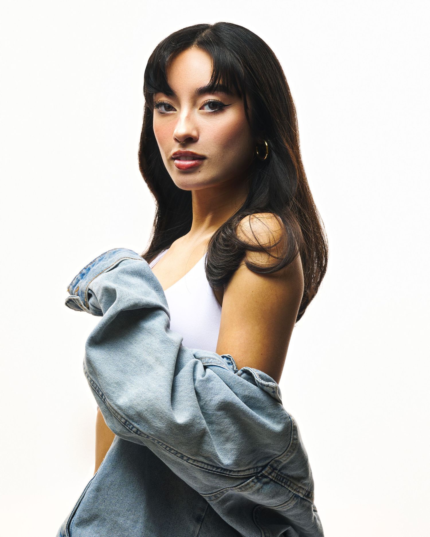 Portrait shot with denim jacket and white tank top against minimalist background.