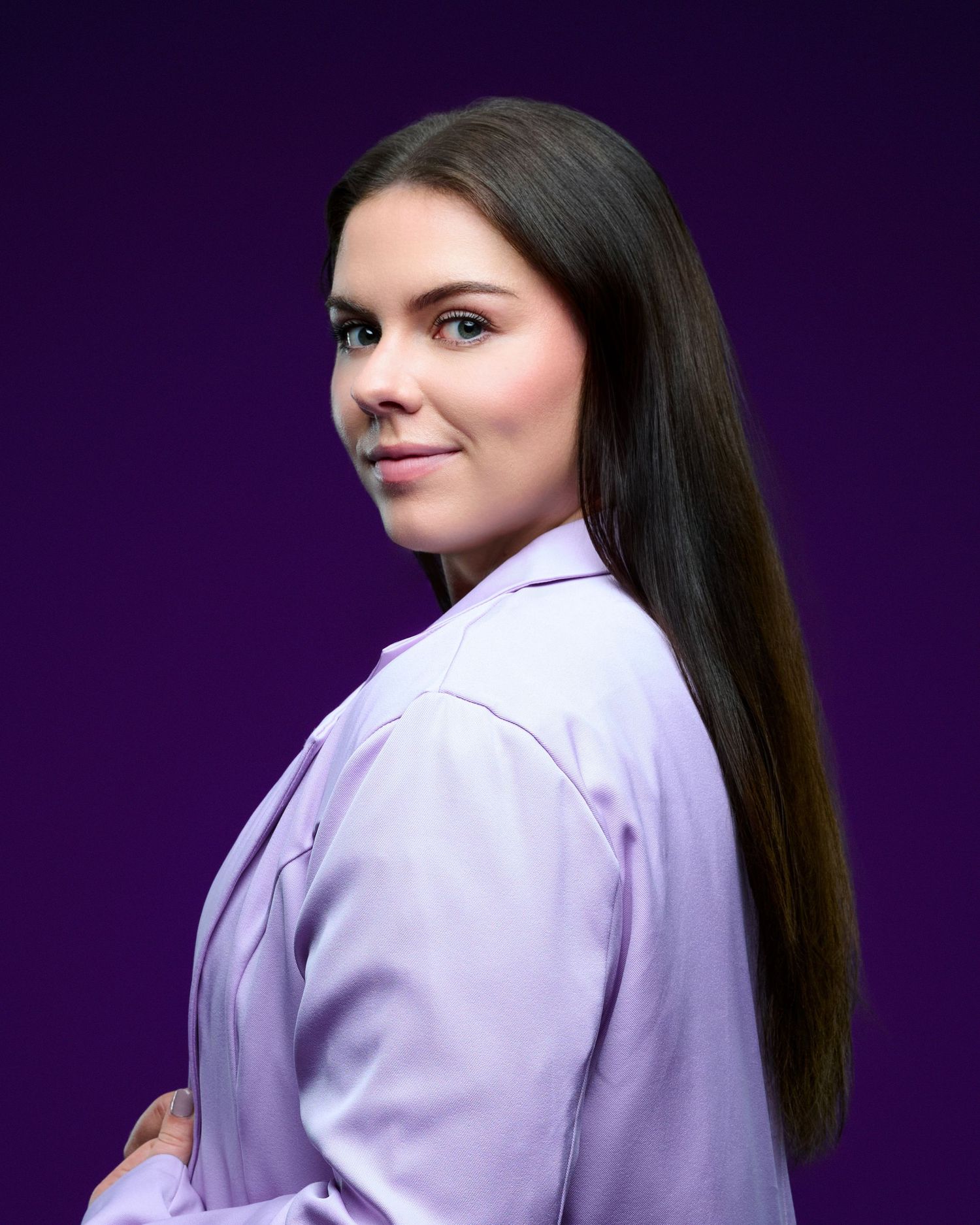 Studio portrait with long dark hair wearing white jacket against purple background.