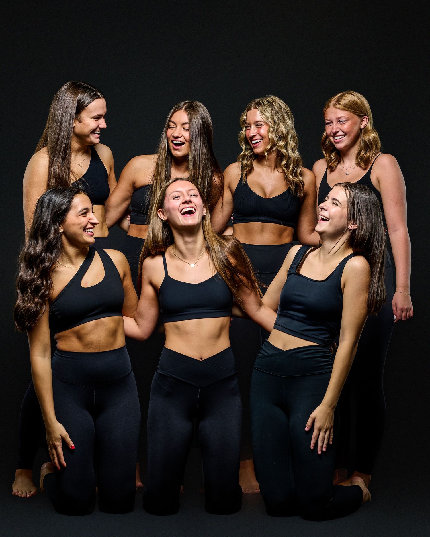 Dancers in black athletic wear laughing together during casual photo session.