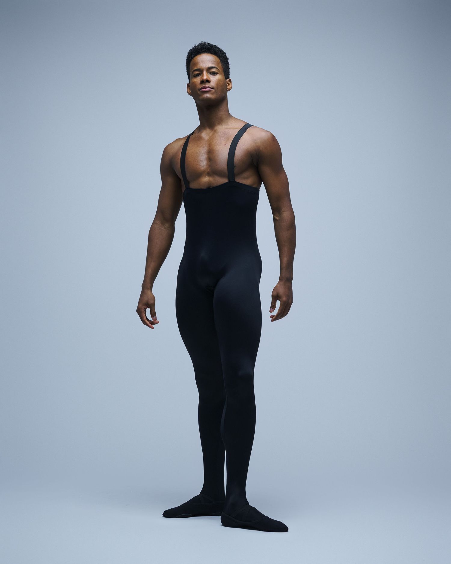 Dance performer wearing black unitard poses professionally in studio setting.