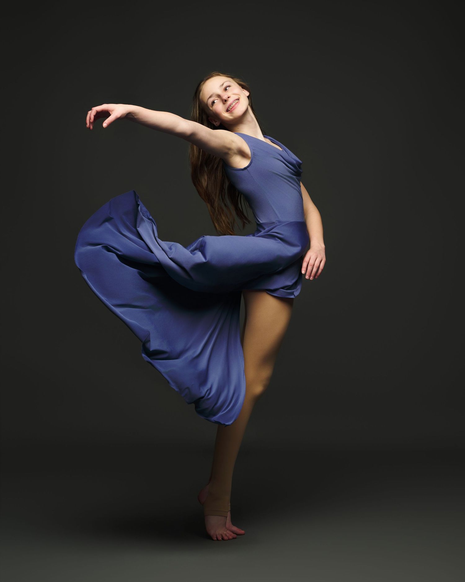 A dancer in blue performs a graceful movement with flowing fabric against a dark background.