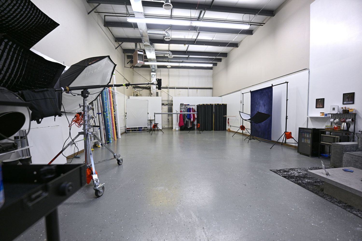 Large empty photography studio space with lighting equipment and gray flooring.