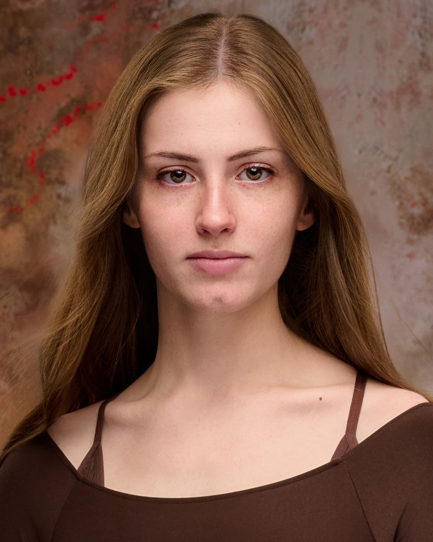 Portrait with long straight blonde hair wearing brown top against textured background.
