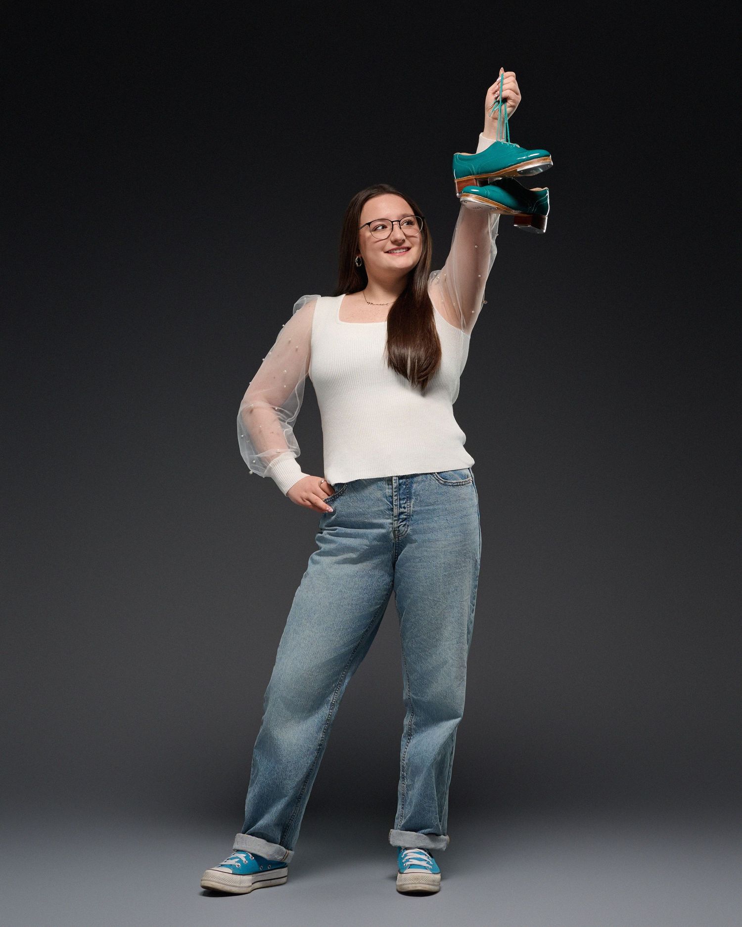 A studio portrait of someone in casual wear holding up a green sneaker against a dark background.
