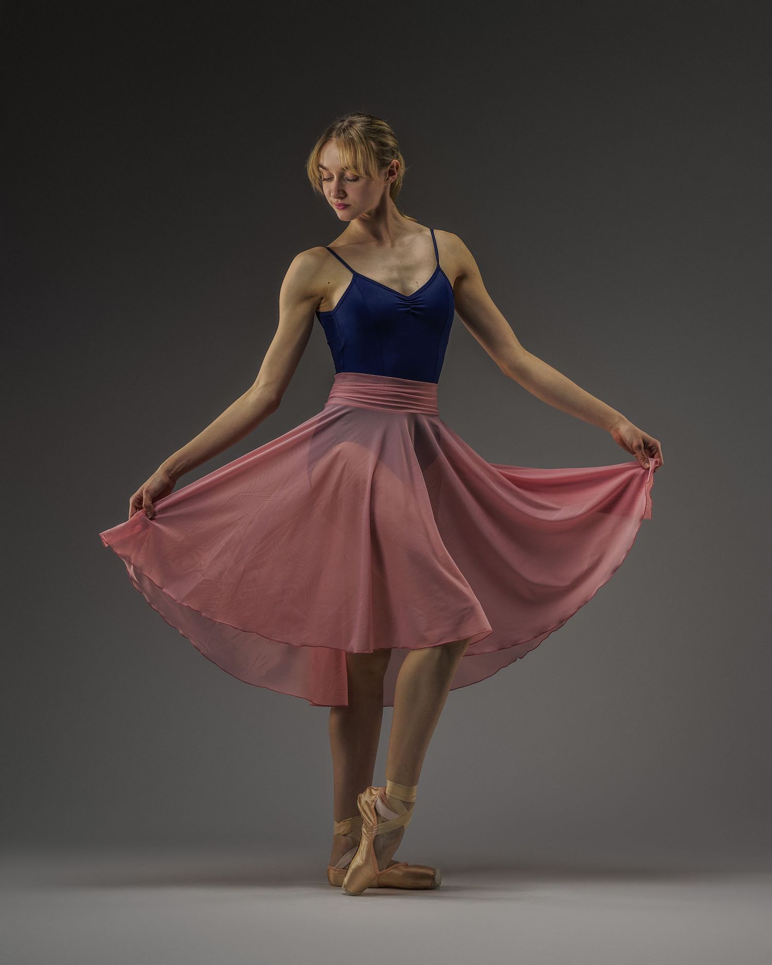 Ballet dancer in navy leotard and pink skirt poses elegantly on pointe shoes.