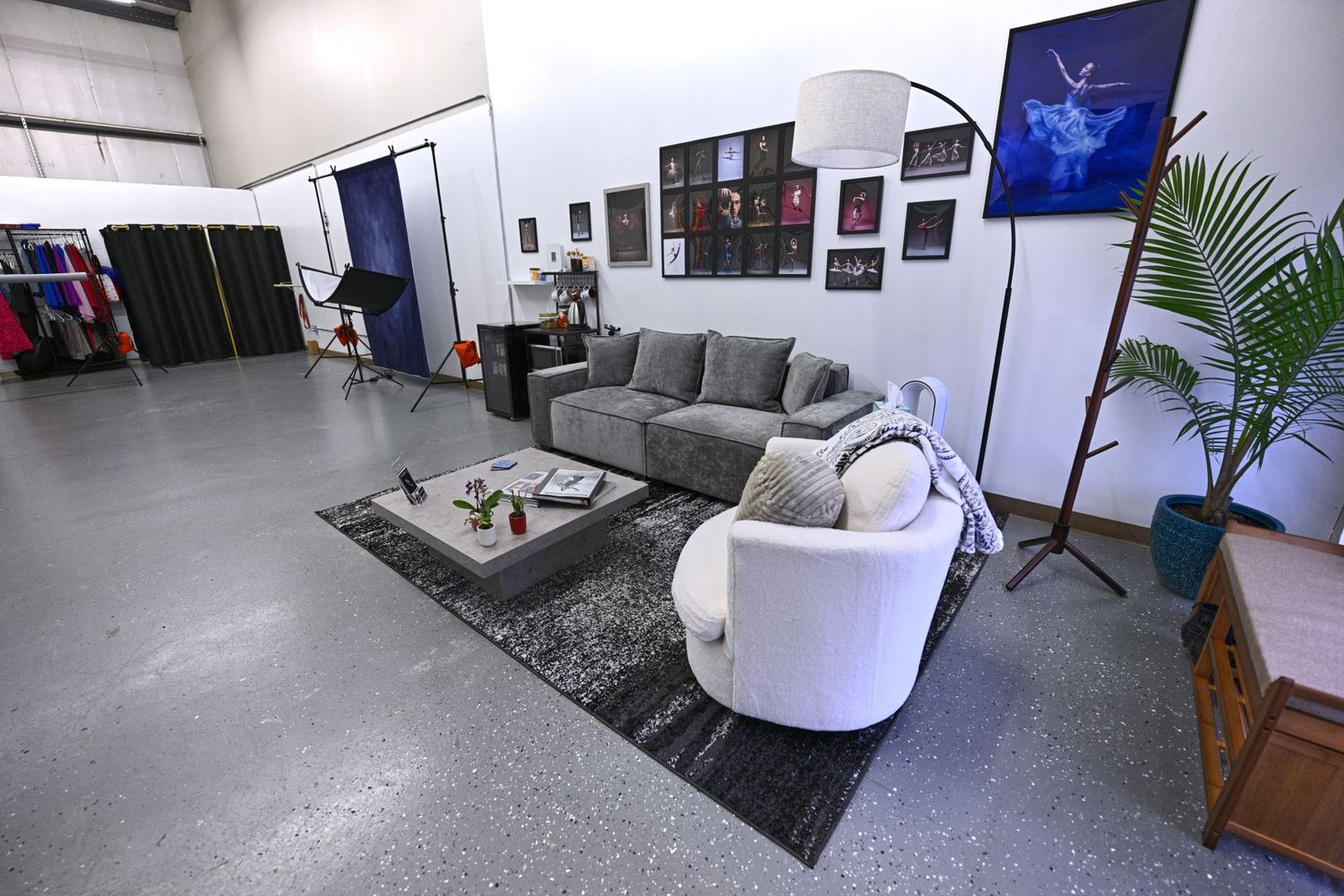 Modern studio lounge area with gray couch, white chairs, and decorative elements on concrete floor.
