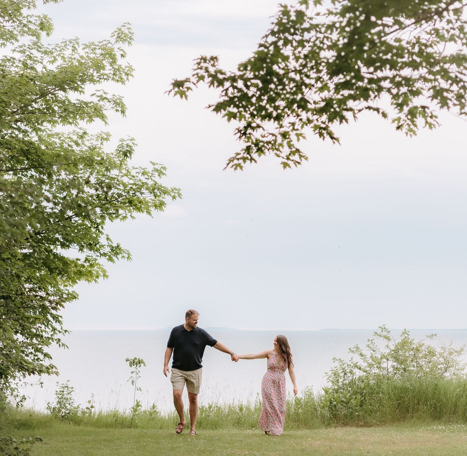 Couple walking through a scenic green field under summer sky.