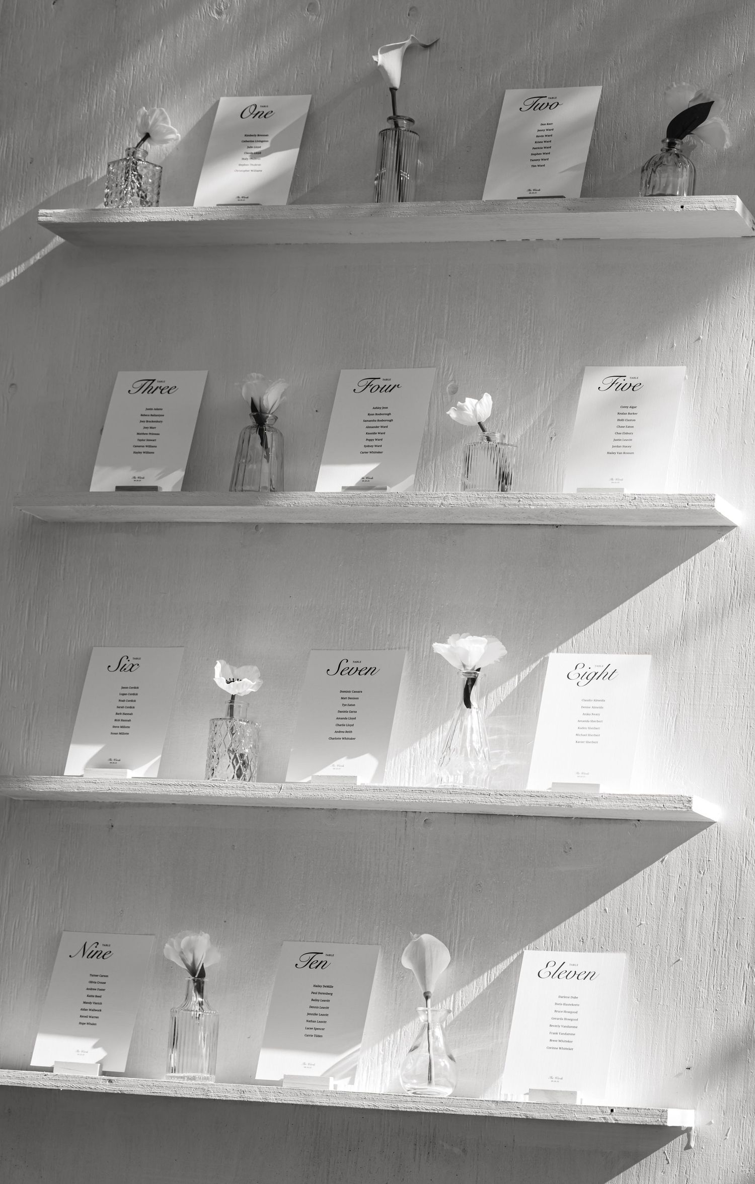 Wedding seating cards displayed on white shelves against a light wall.