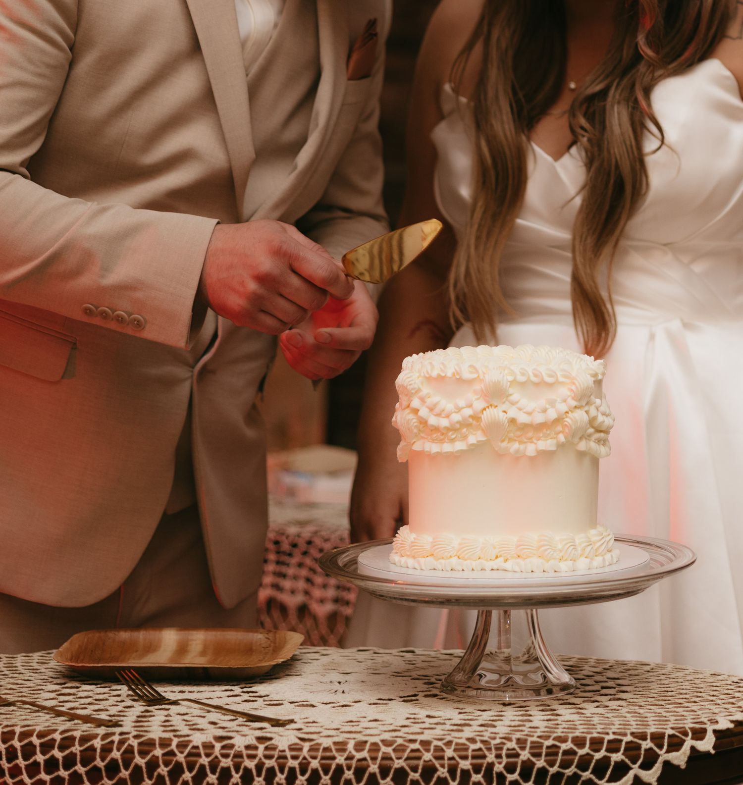 Bride and groom cutting elegant white wedding cake at reception table.