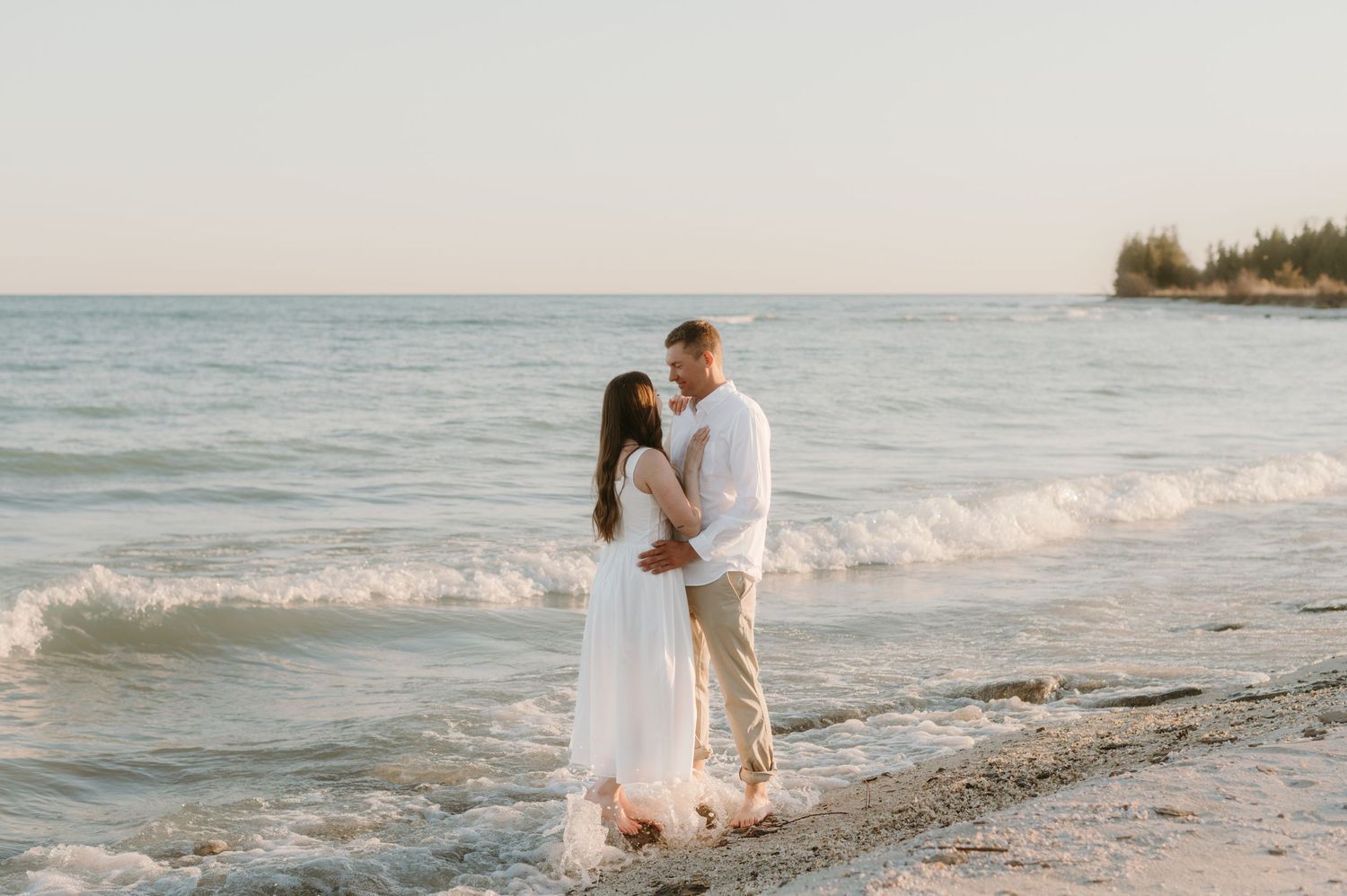 A couple embracing on a peaceful beach with gentle waves in the background.