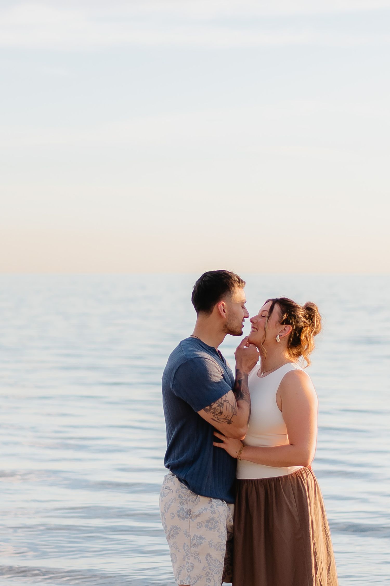 A couple shares a romantic moment together on a beach at sunset with calm ocean waters in the background  in Prince Edward County