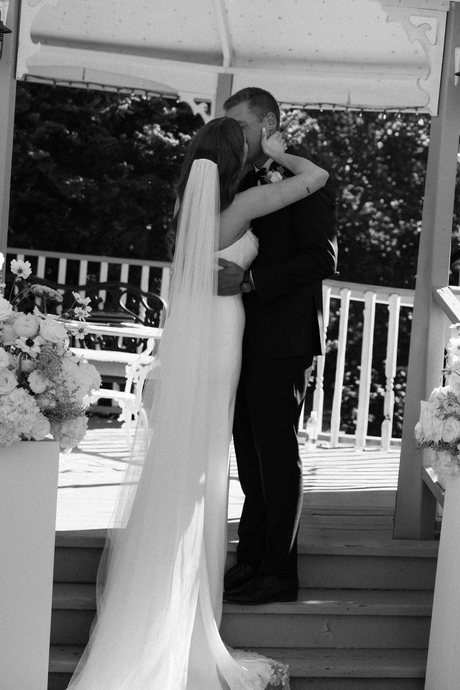Black and white photo of bride and groom sharing first kiss at altar.