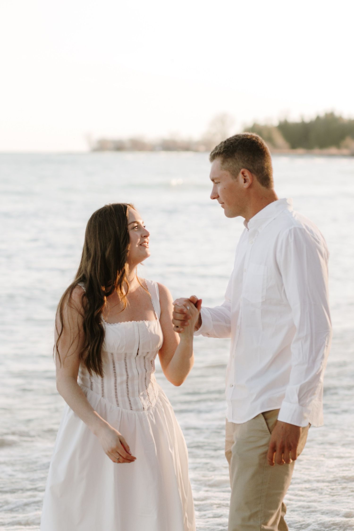 Couple dressed in white sharing intimate moments on a beach at golden hour.