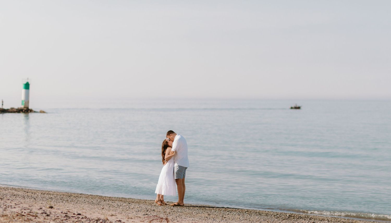 A romantic beach photoshoot with a green lighthouse visible in the distance.
