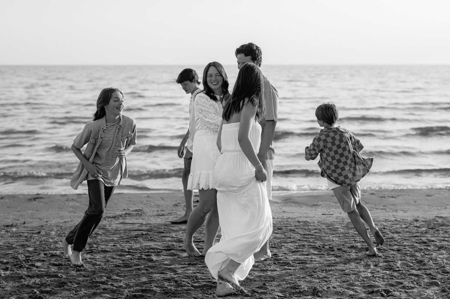 Family enjoying a playful moment together walking along a black and white beach at sunset.