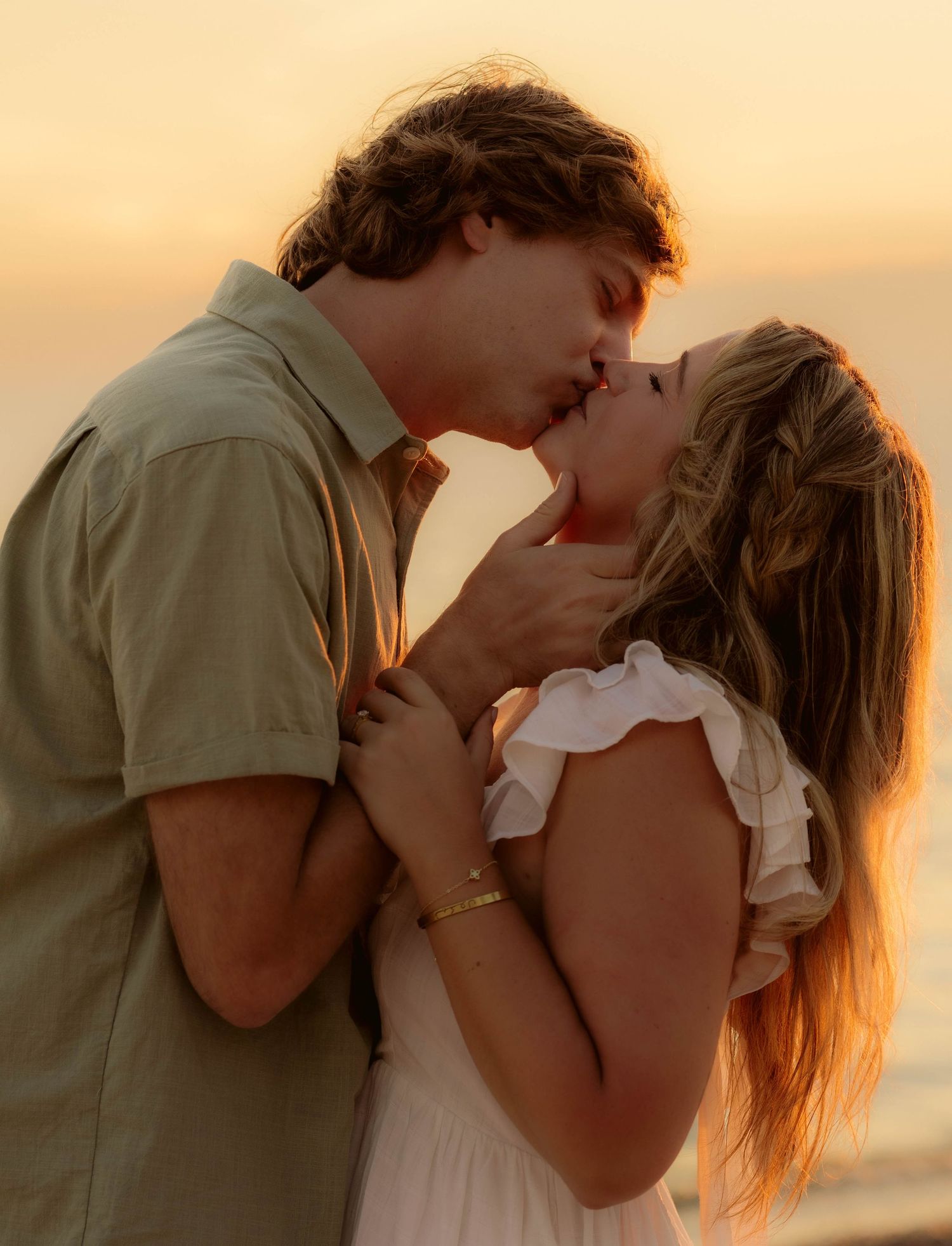 A couple shares a romantic sunset kiss on the beach, the golden light illuminating their embrace.
