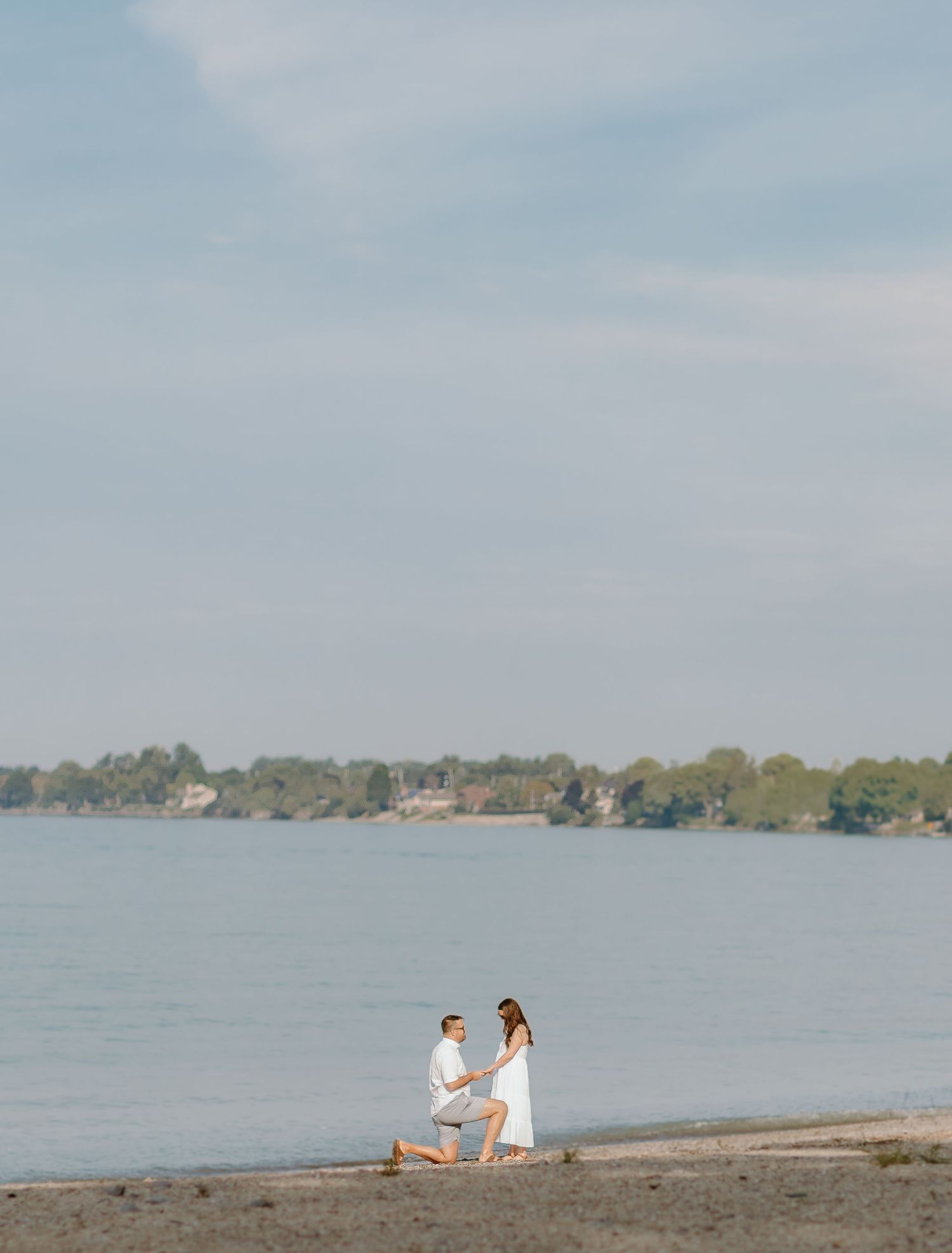 Marriage proposal scene taking place on a scenic lakefront with trees in the background.