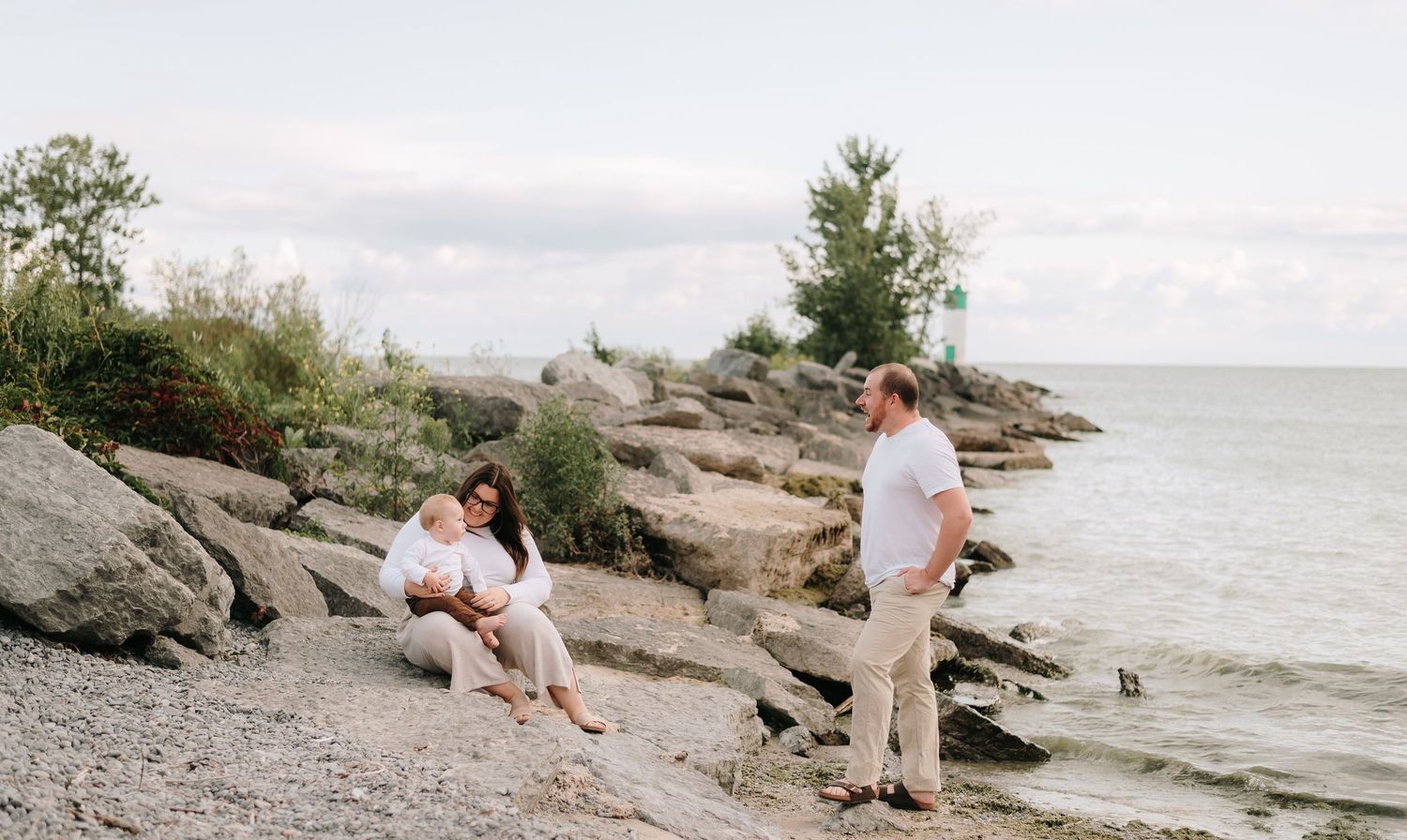 People sit on rocky coastal shore overlooking the ocean on a cloudy day.