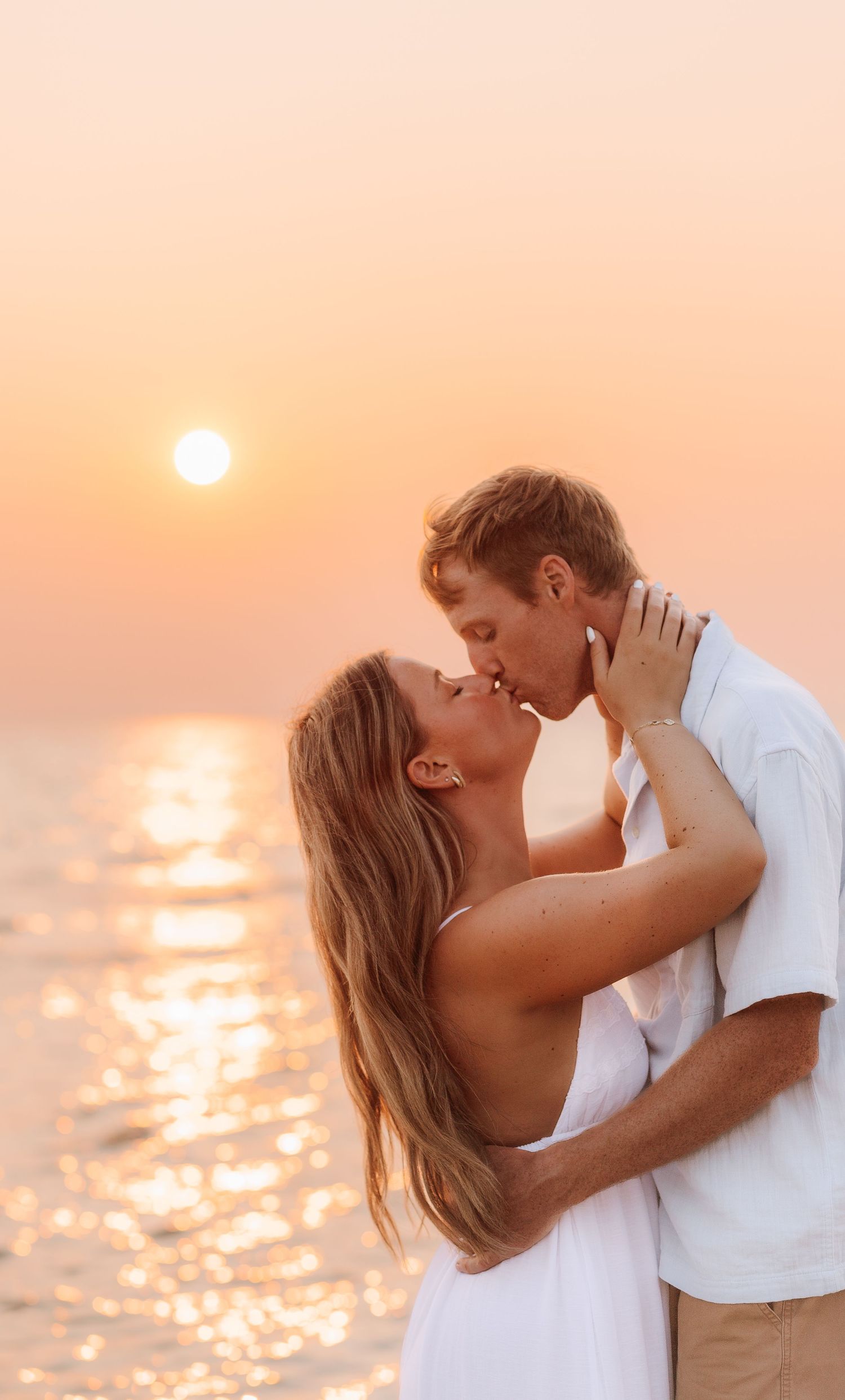 Couple sharing a romantic kiss on the beach at sunset, with golden light reflecting on the ocean water.