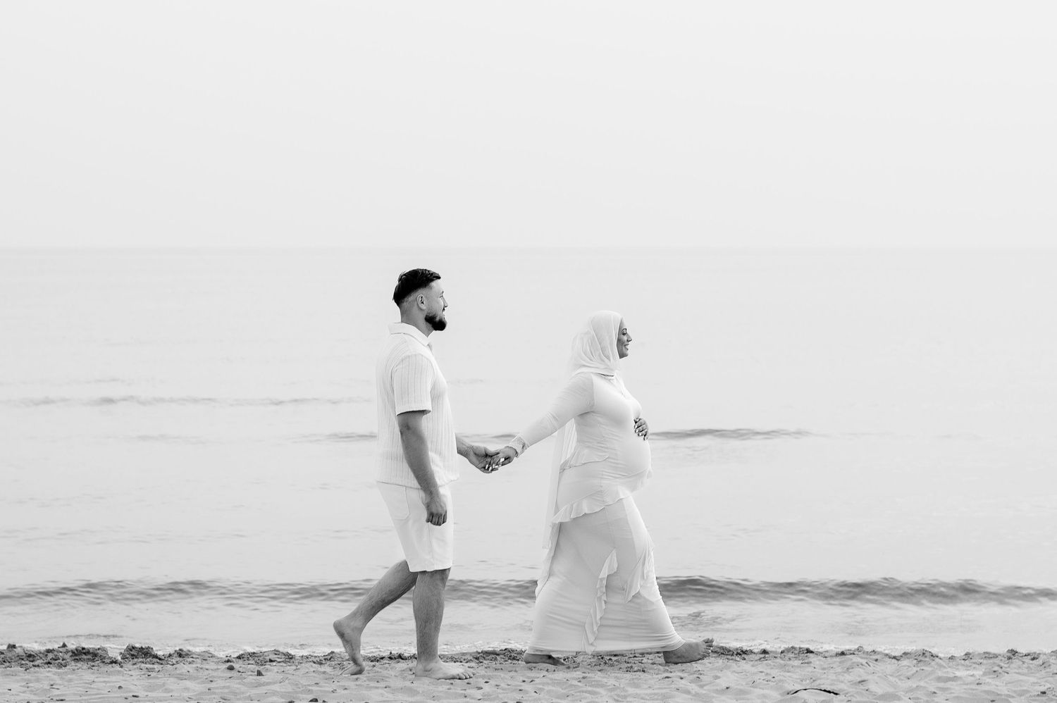 A romantic black and white photo series of a couple walking and dancing together on a beach  in Prince Edward County