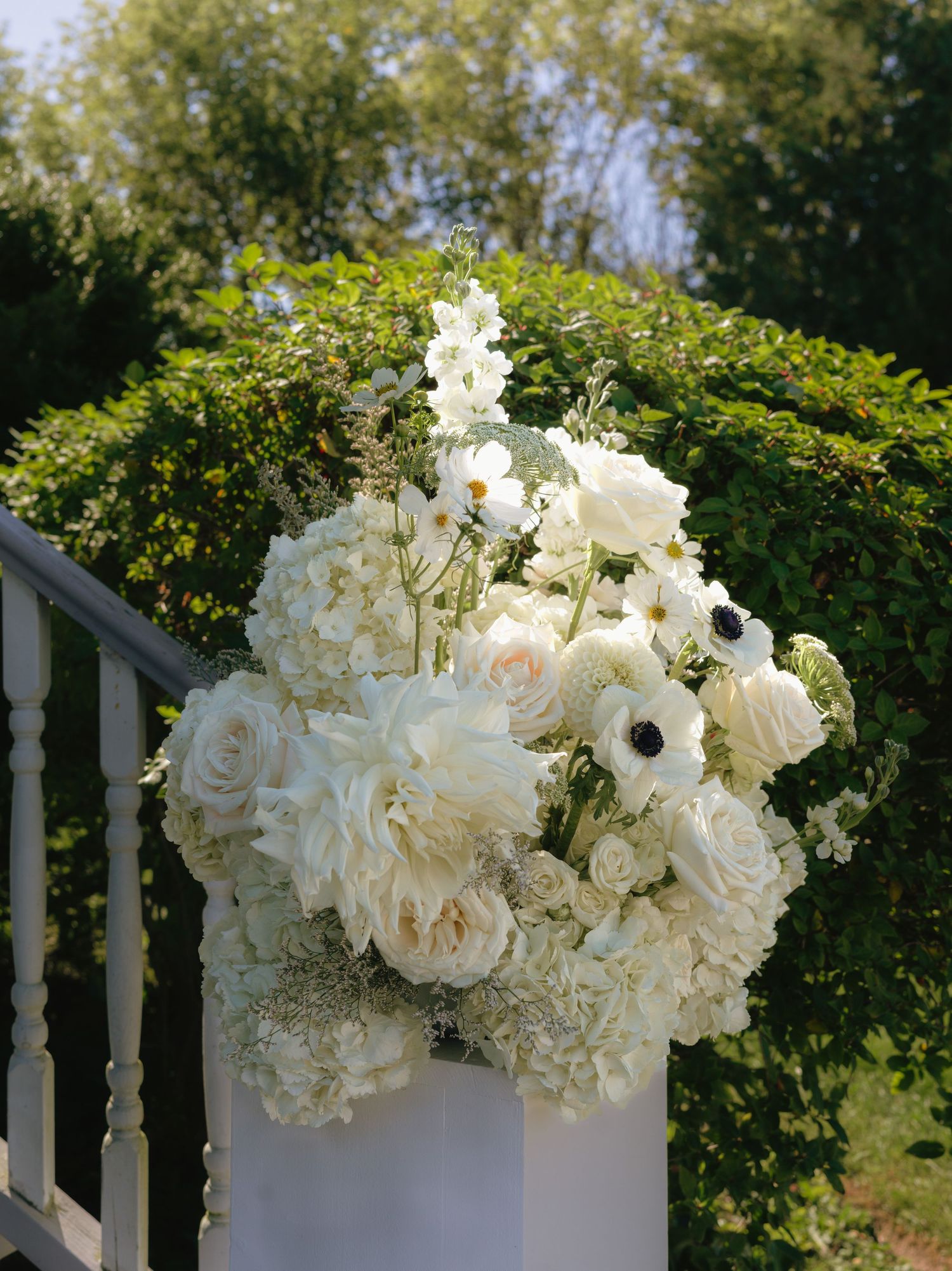 White floral arrangements with roses and hydrangeas decorating an outdoor railing in Prince Edward County