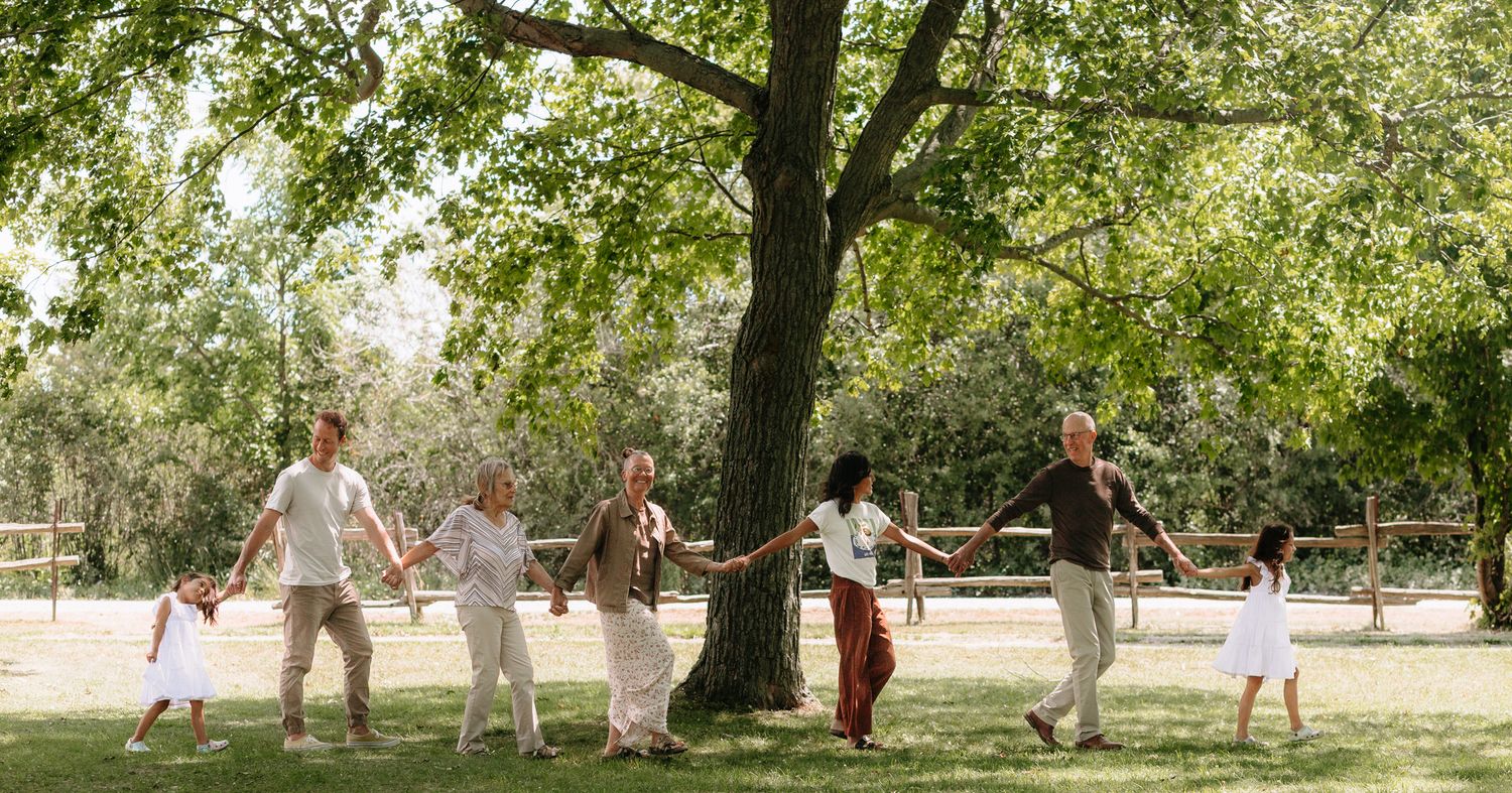 A panoramic view of a family gathering under large shady trees in a park in Prince Edward County