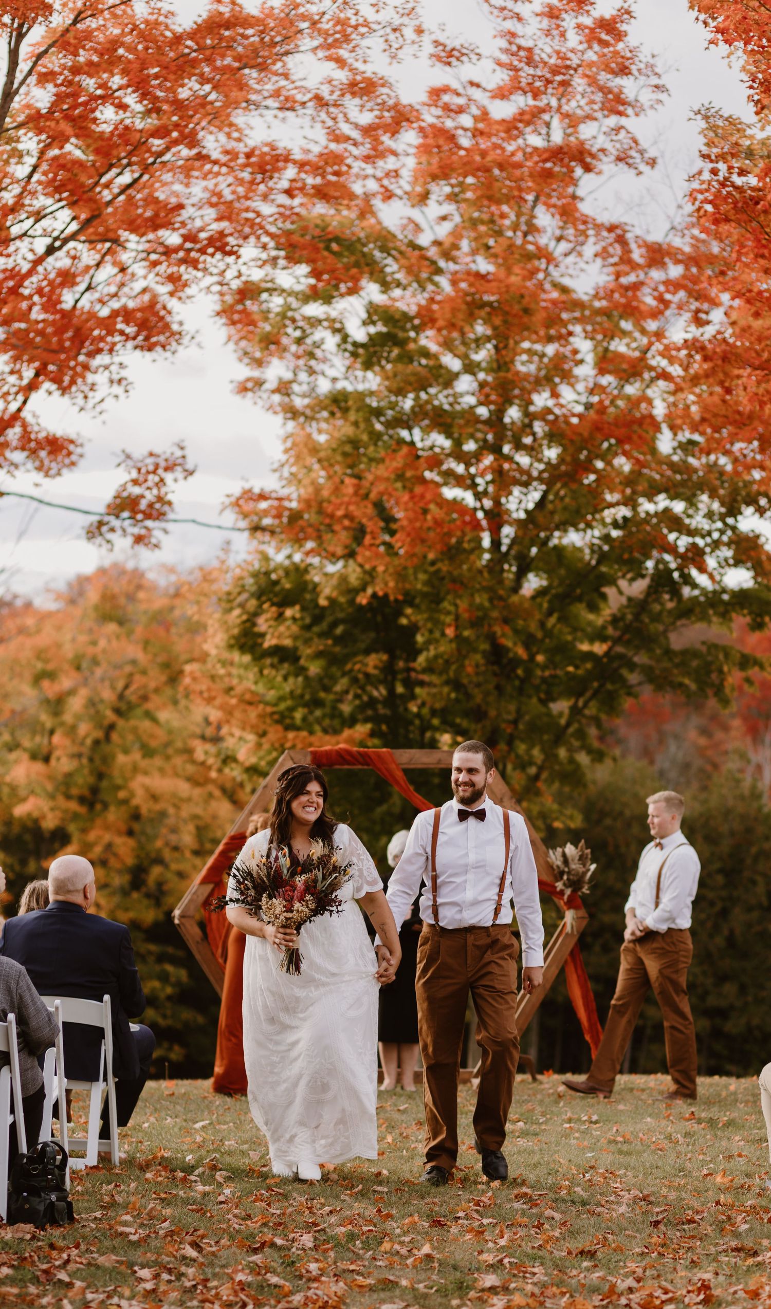 Bride and groom walk down the aisle at an outdoor fall wedding ceremony with vibrant red maple trees.