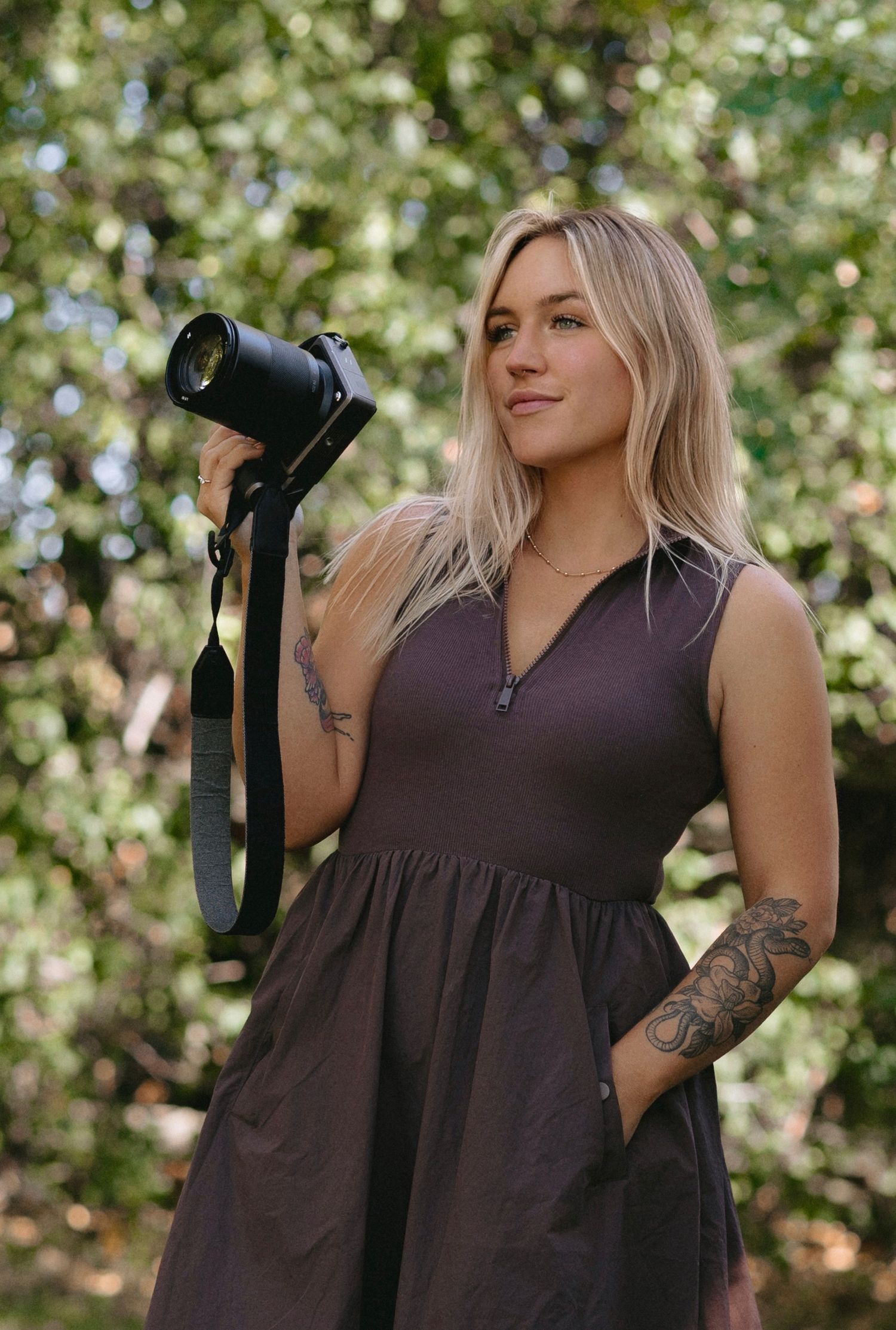 A person in a brown sleeveless dress poses outdoors against a blurred background of white flowering trees.