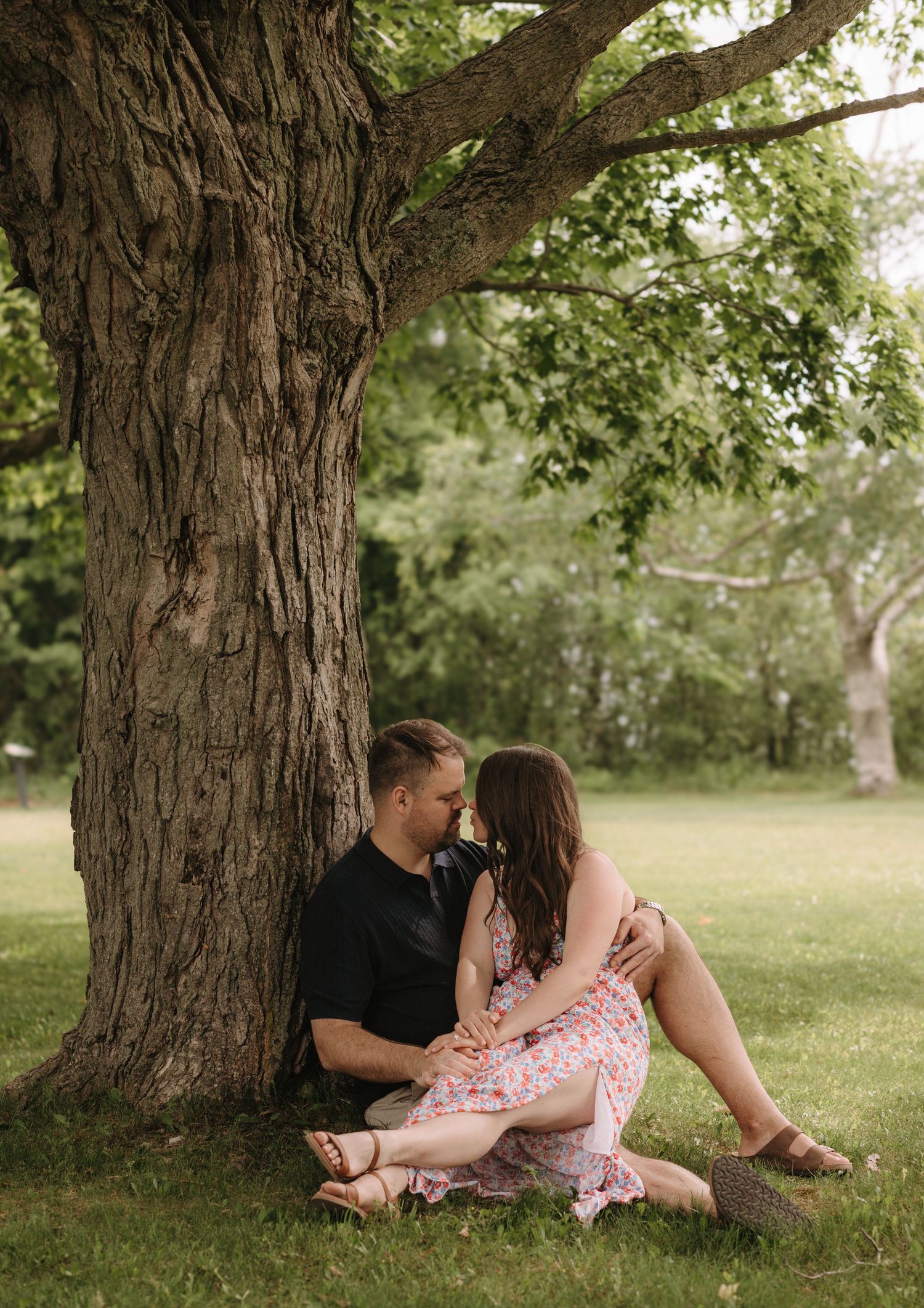 Couple relaxing and sharing intimate moments under a large tree in a park.