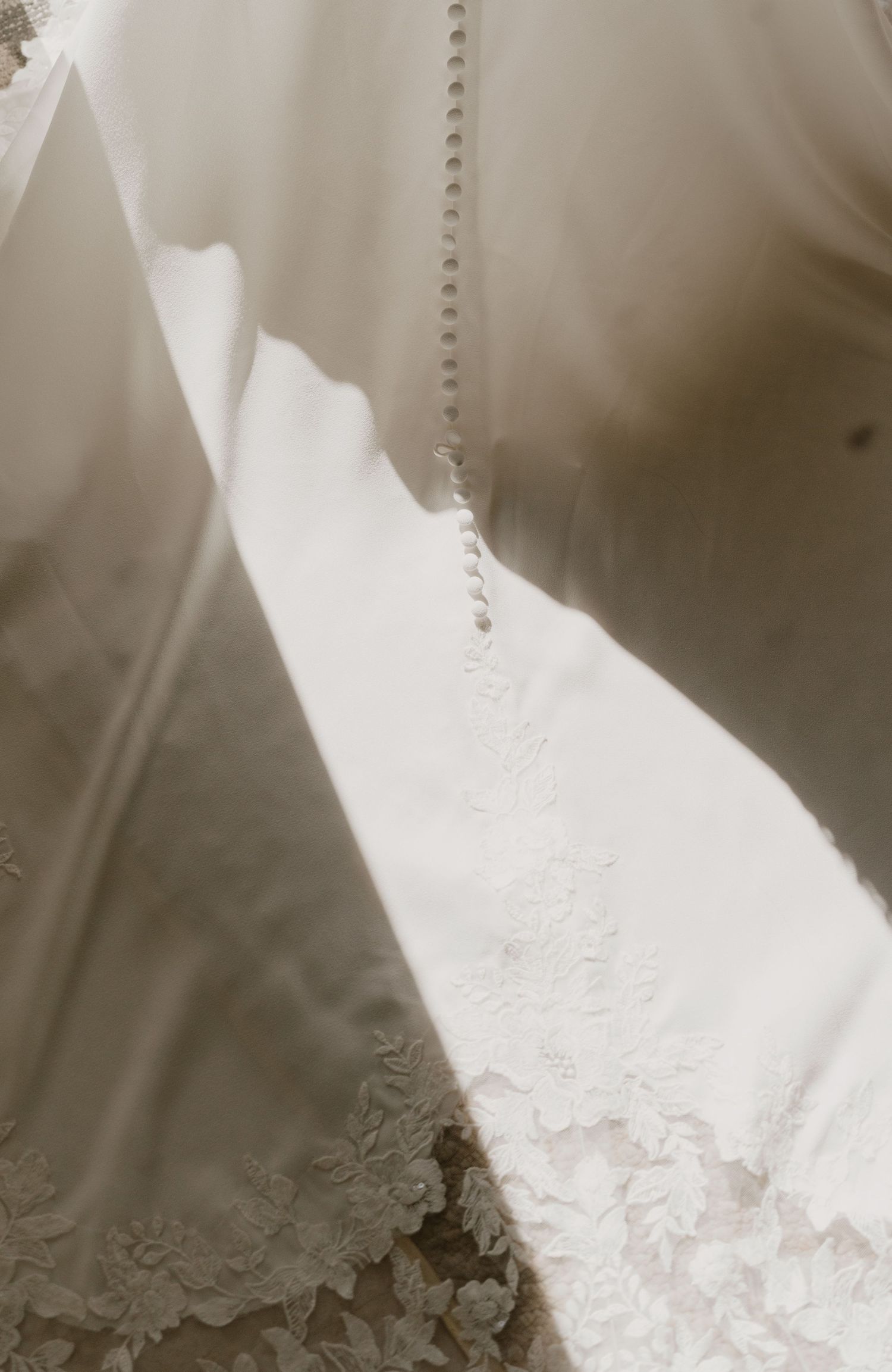 Close-up detail of a wedding dress with delicate lace trim and pearl button back closure.