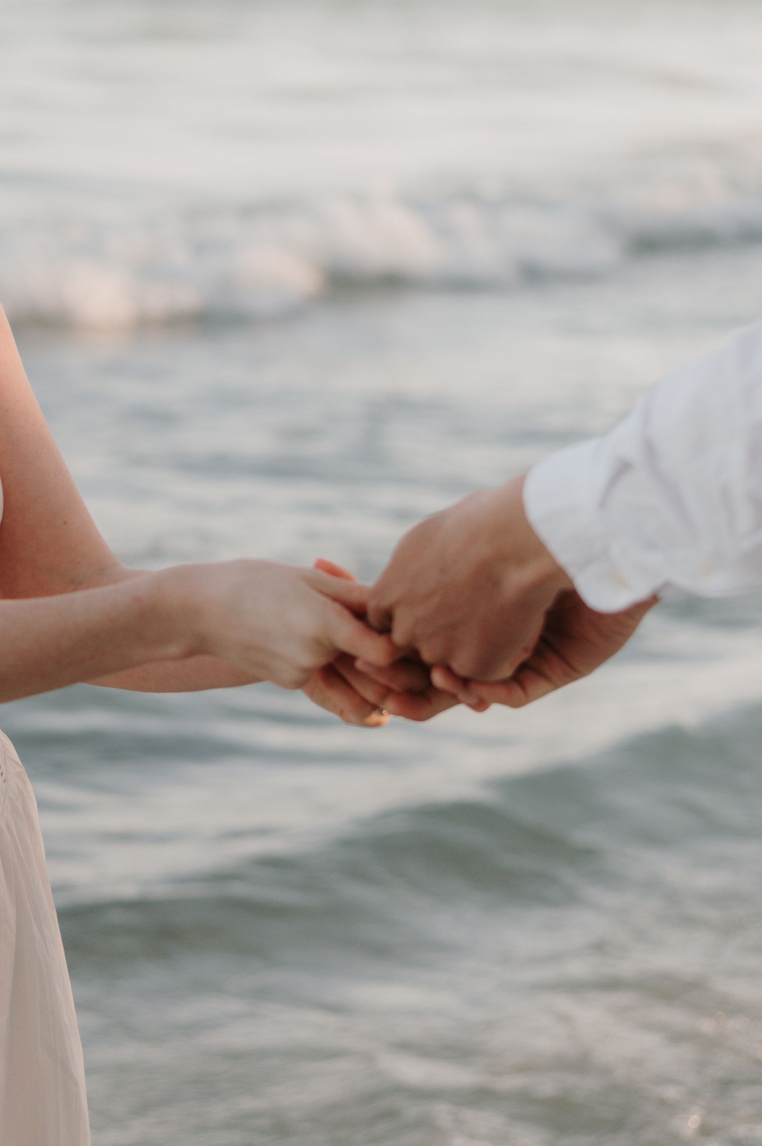 Close up of two hands reaching towards each other against a blurred ocean background at sunset.