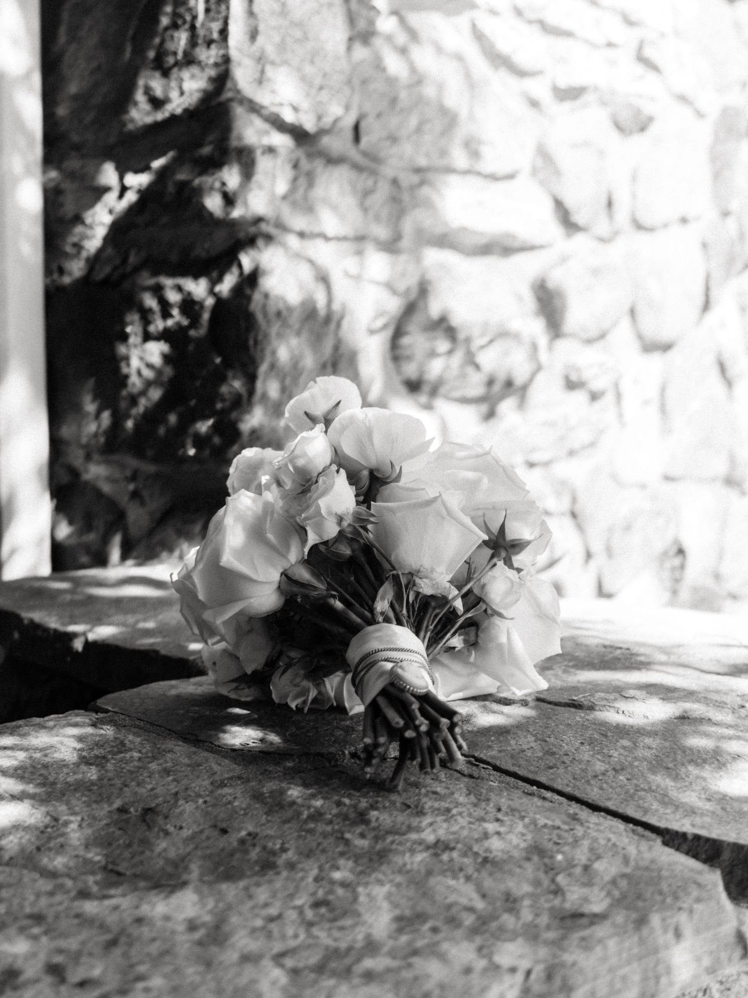 Black and white photo of a bridal bouquet of roses resting on a stone surface.