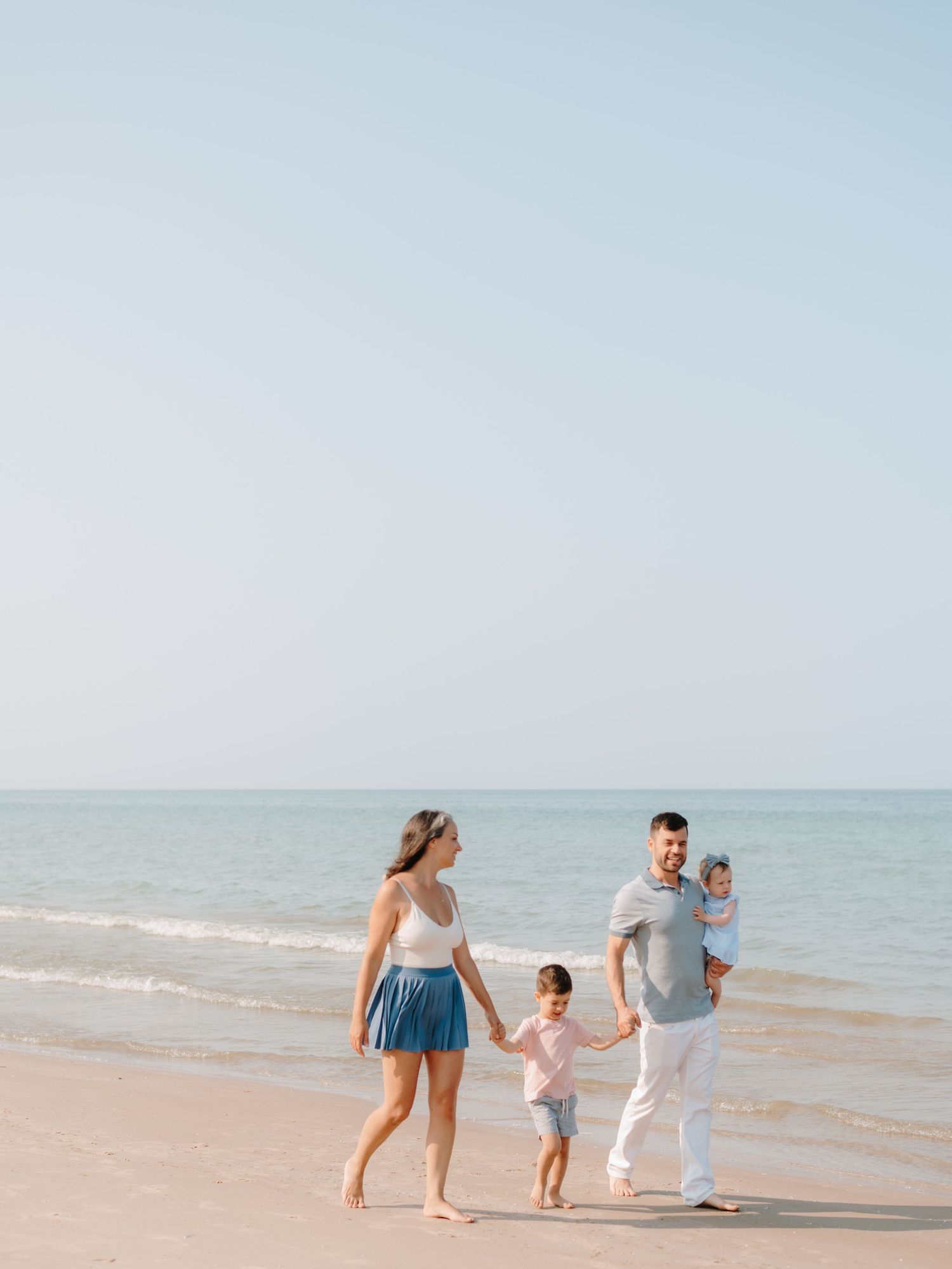 Family walking along the beach shoreline on a sunny day with gentle waves rolling in on Sandbanks Beach in Prince Edward County