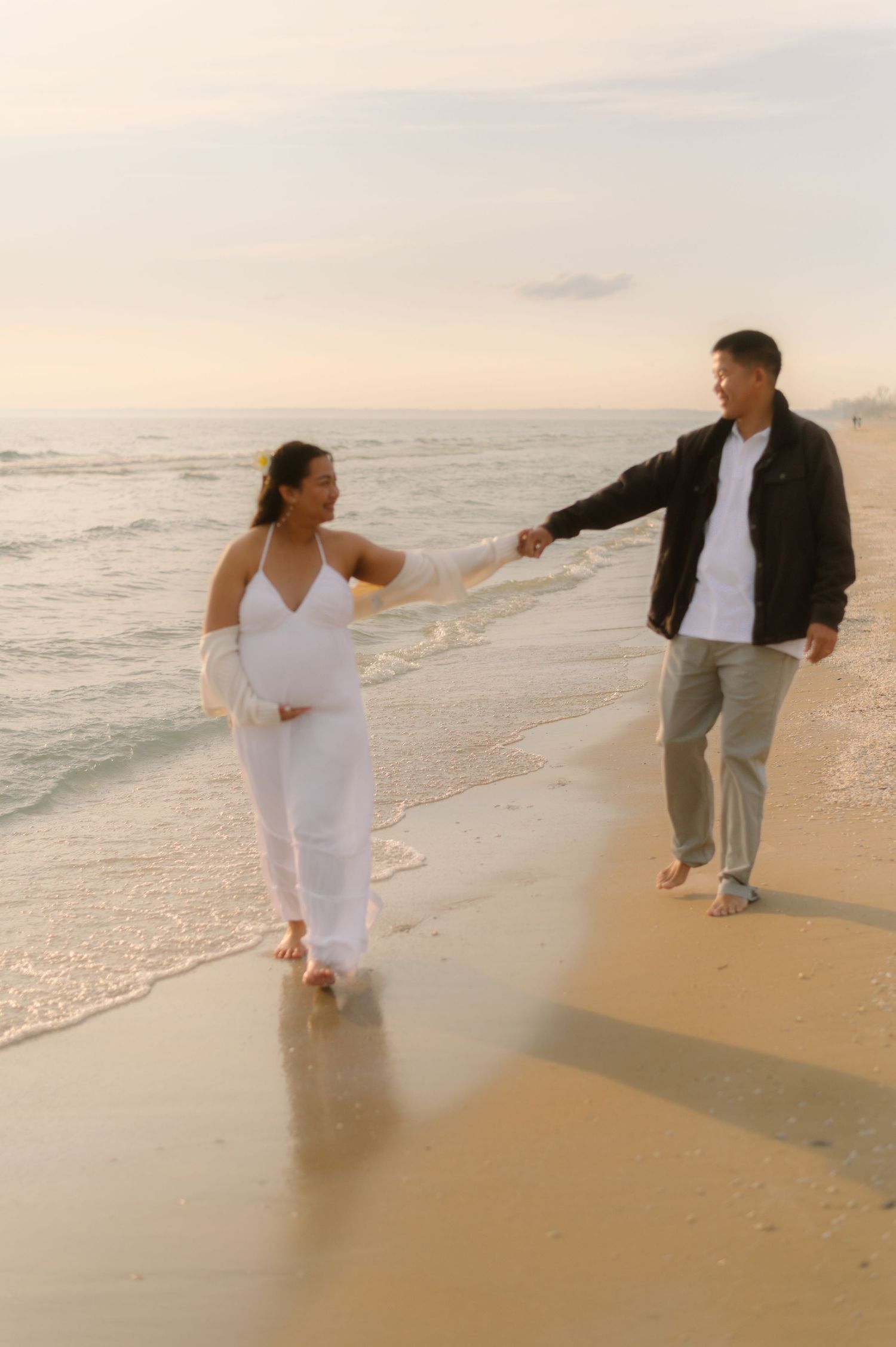 A romantic sunset photoshoot of a couple holding hands and walking along a misty beach shoreline.
