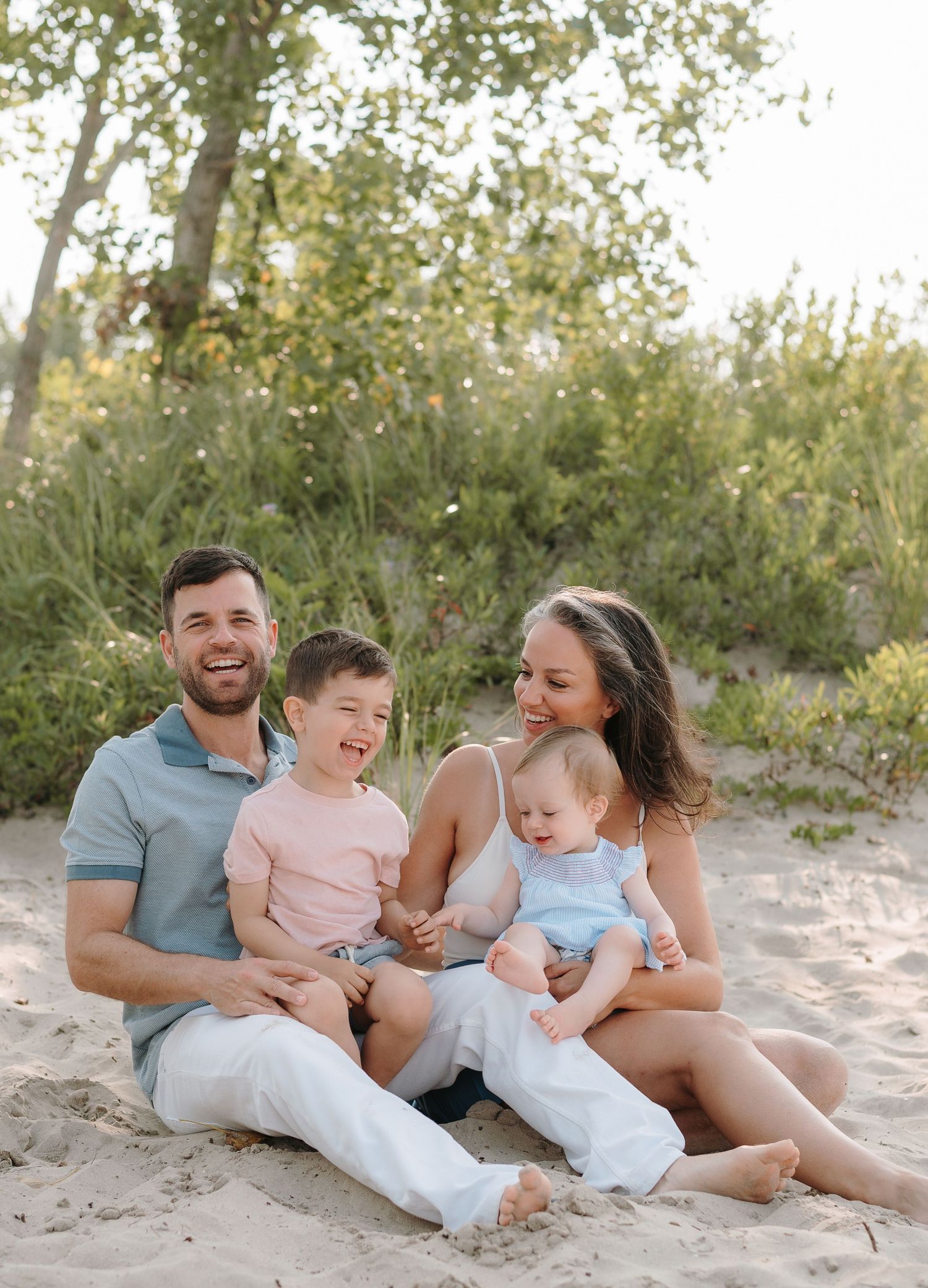 Family relaxing together on sandy beach during sunset photo session in Prince Edward County