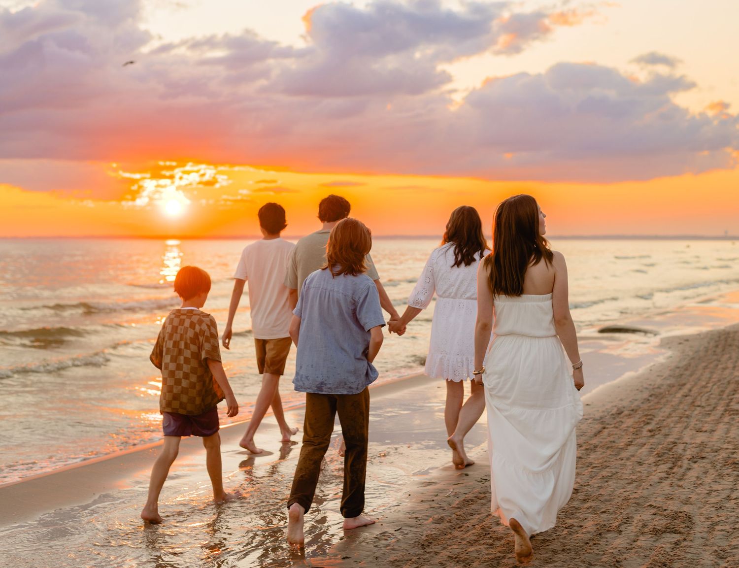 A group of people walking together on a sandy beach at sunset with vibrant orange sky over the ocean.