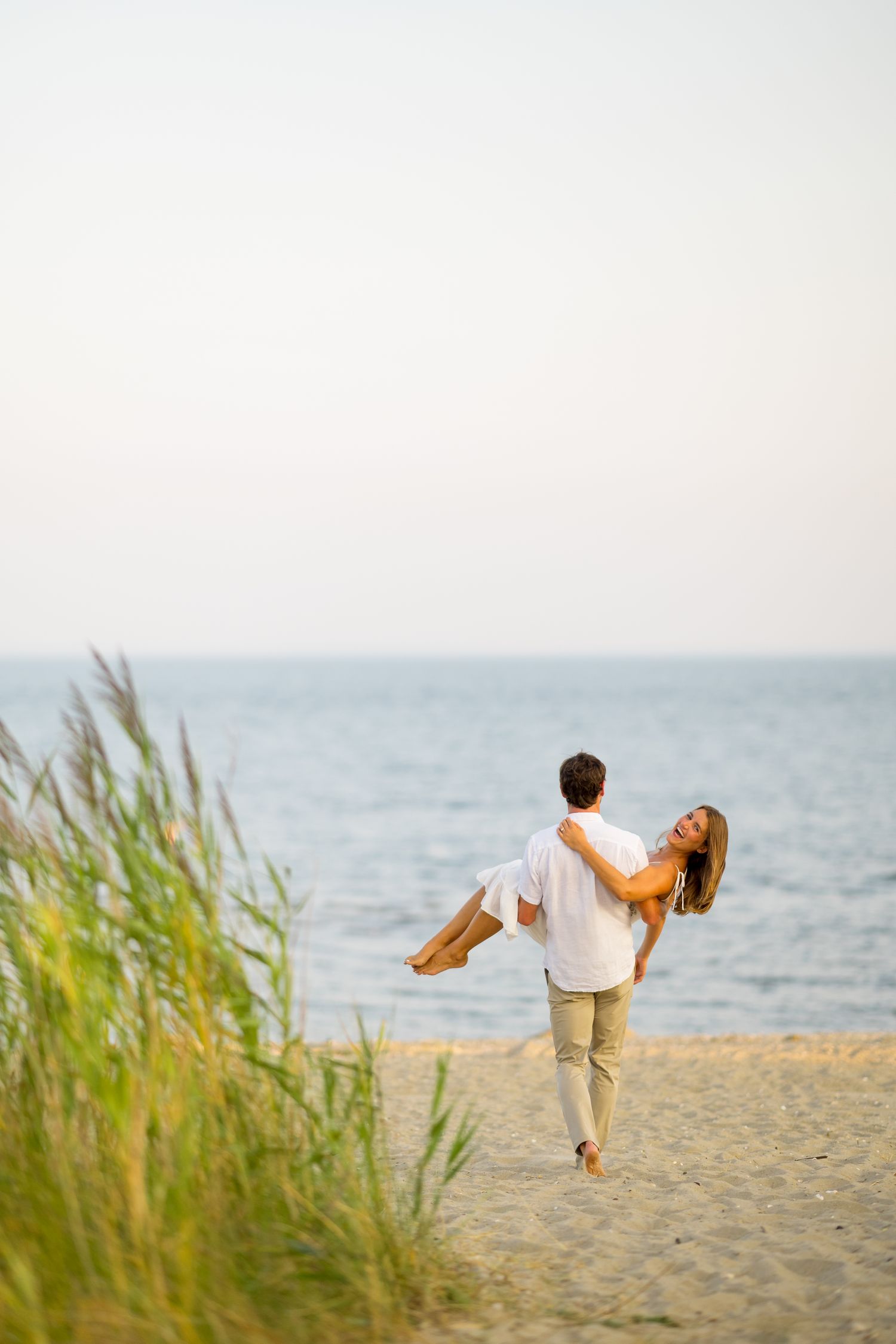 A couple poses playfully on a sandy beach with ocean waves in the background at sunset.