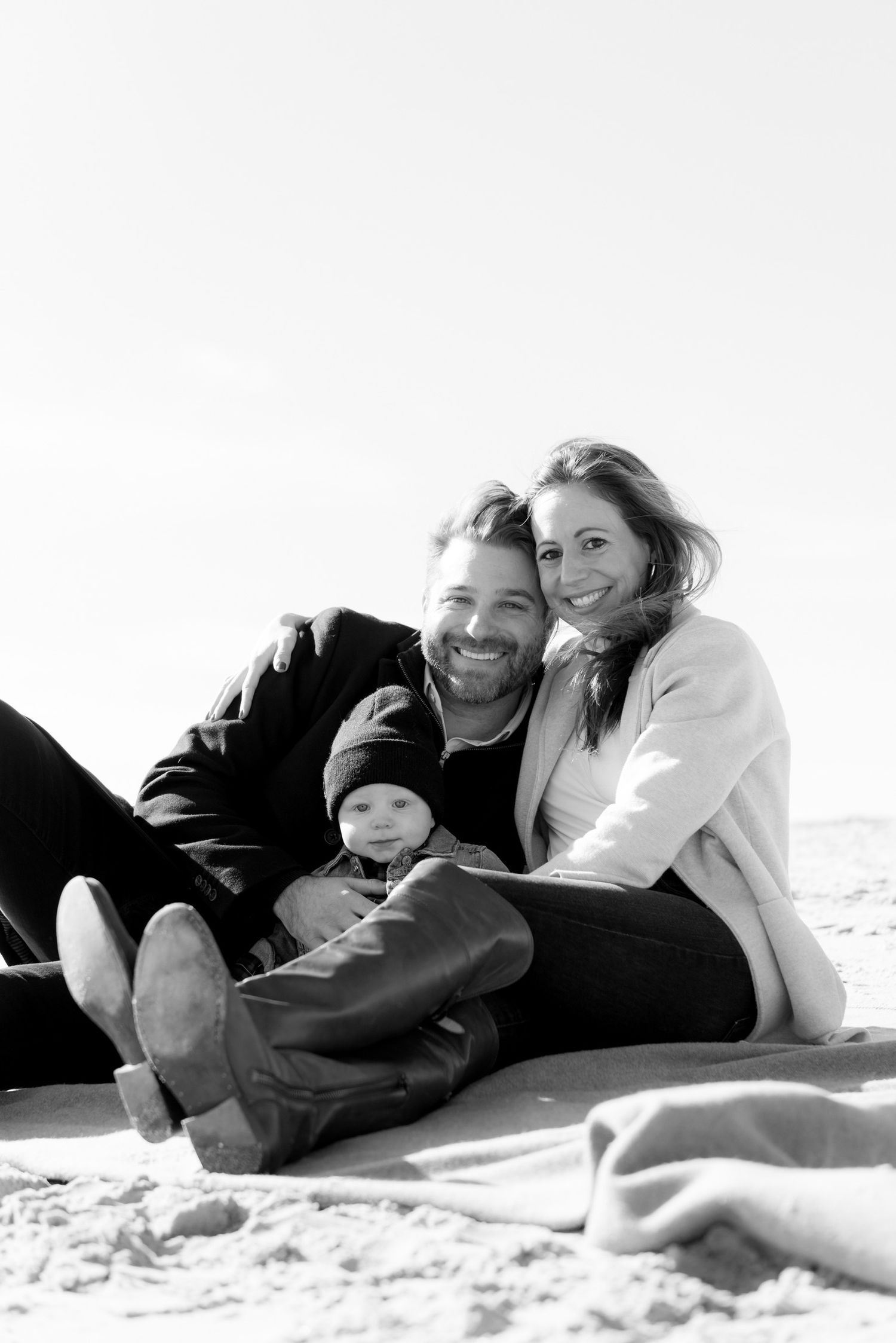 Family lying together on white sand beach in black and white.
