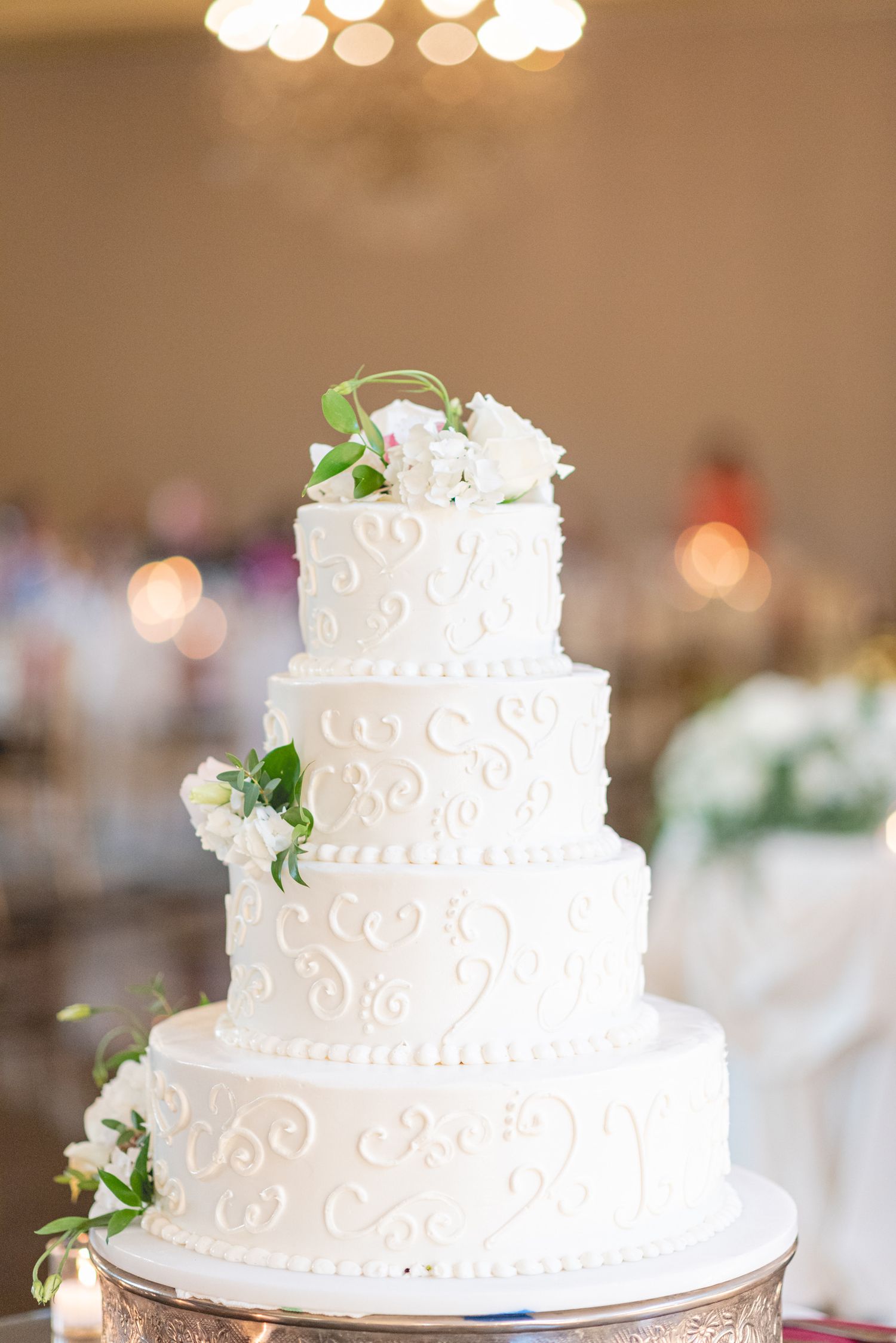 Elegant white tiered wedding cake with delicate swirl designs and floral accents.