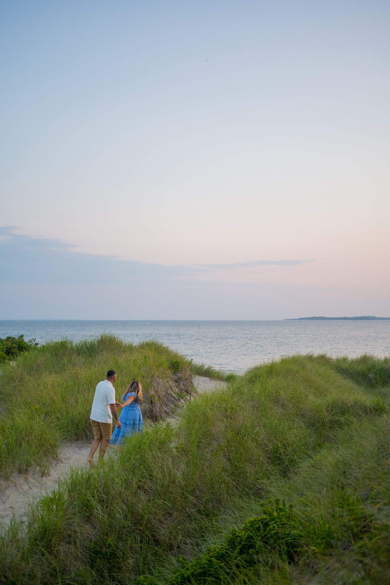 People walking along a grassy coastal path at sunset with ocean views.
